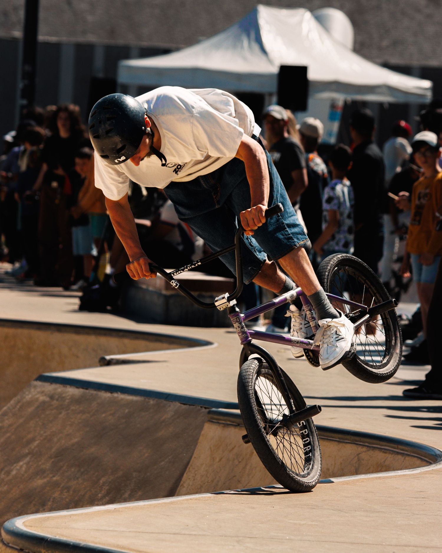 BMX rider performing aerial maneuver on wooden ramp at outdoor competition.