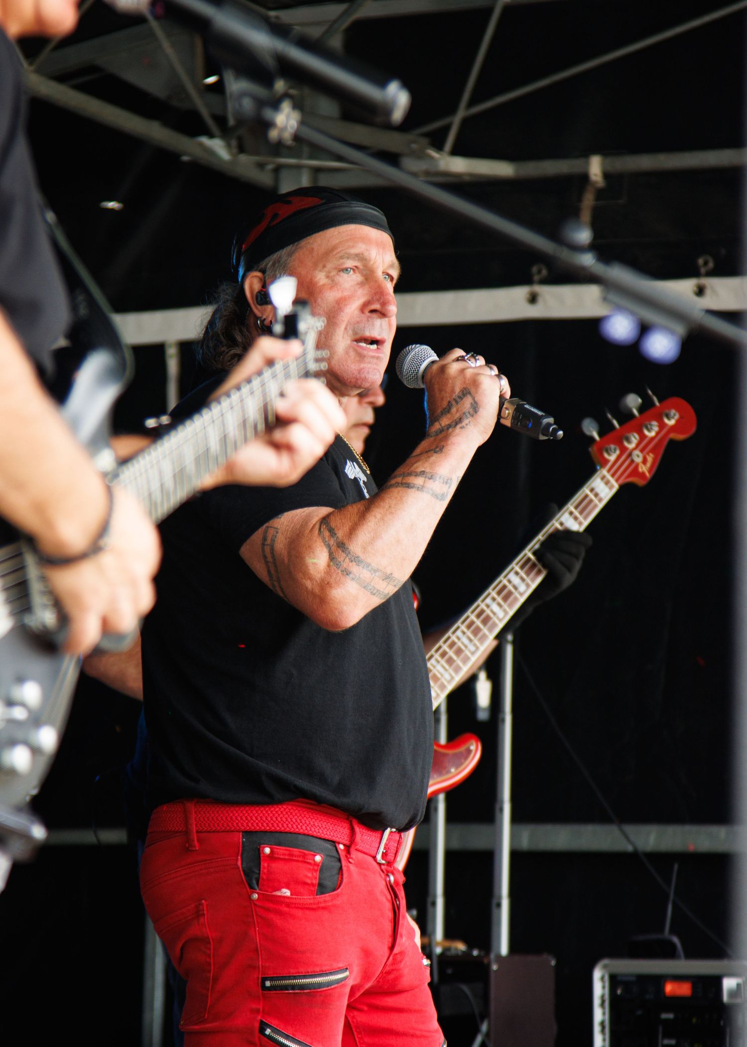 Musician performing energetically with a red guitar on an outdoor stage.