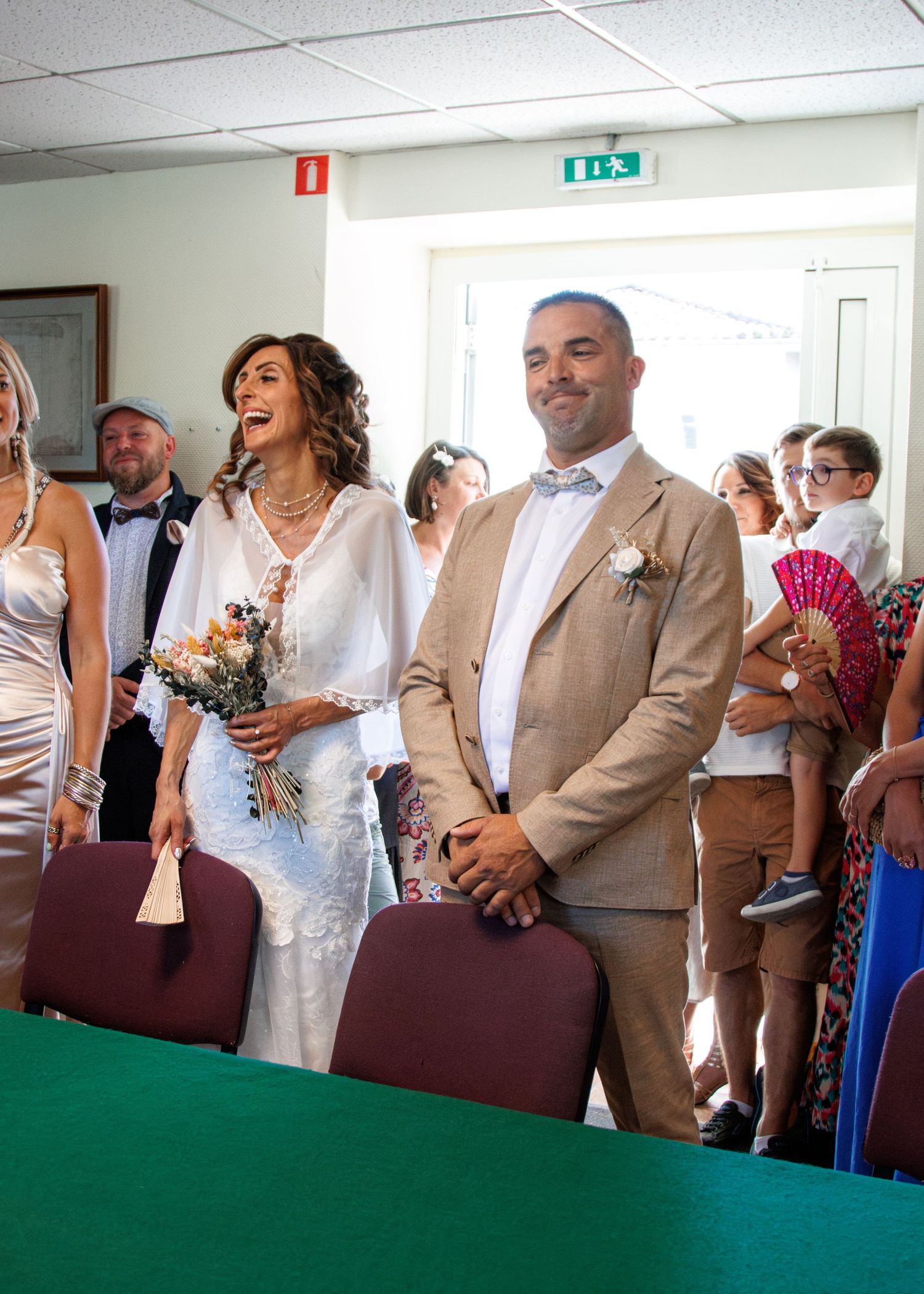 A joyful wedding couple stands together at their ceremony while guests watch and smile in the background.