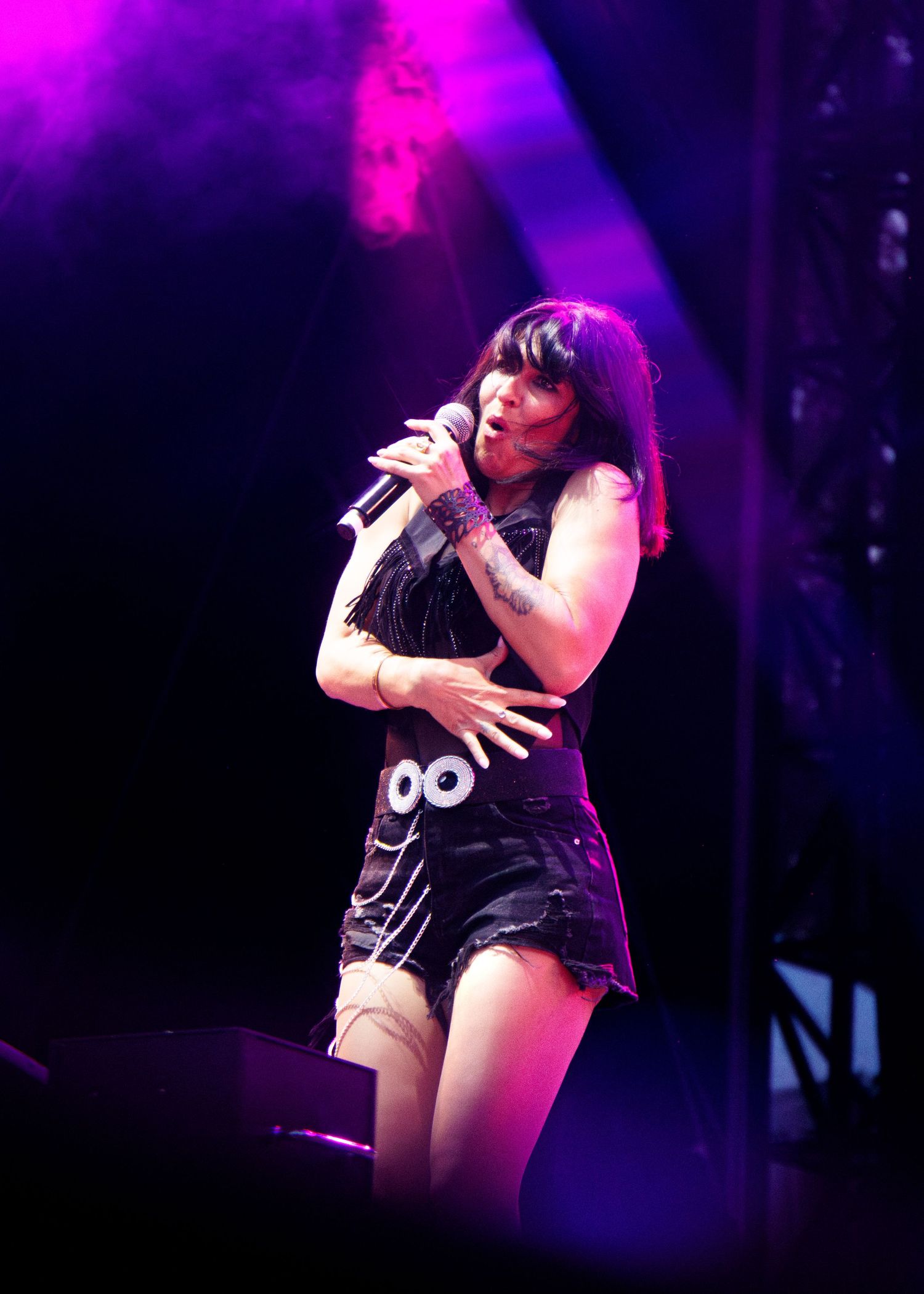A performer in a black outfit sings emotively on stage under vibrant purple lighting at a concert performance.