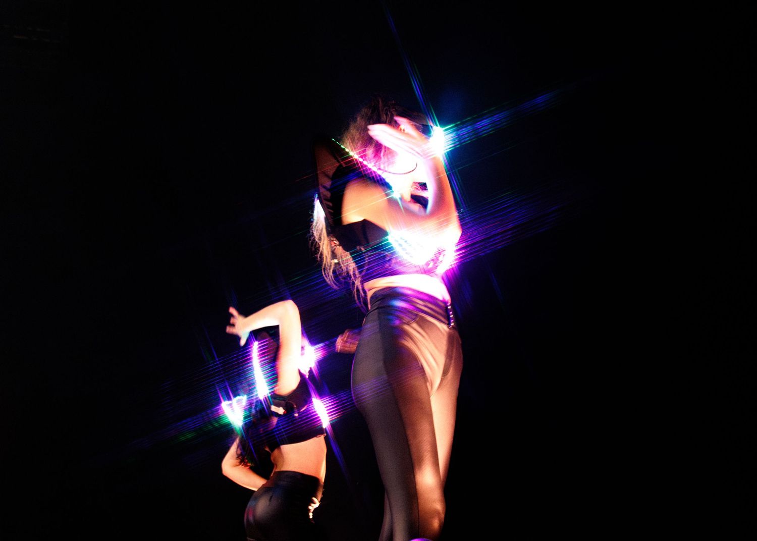 A person in dramatic pose illuminated by pink and blue lights on a dark stage.