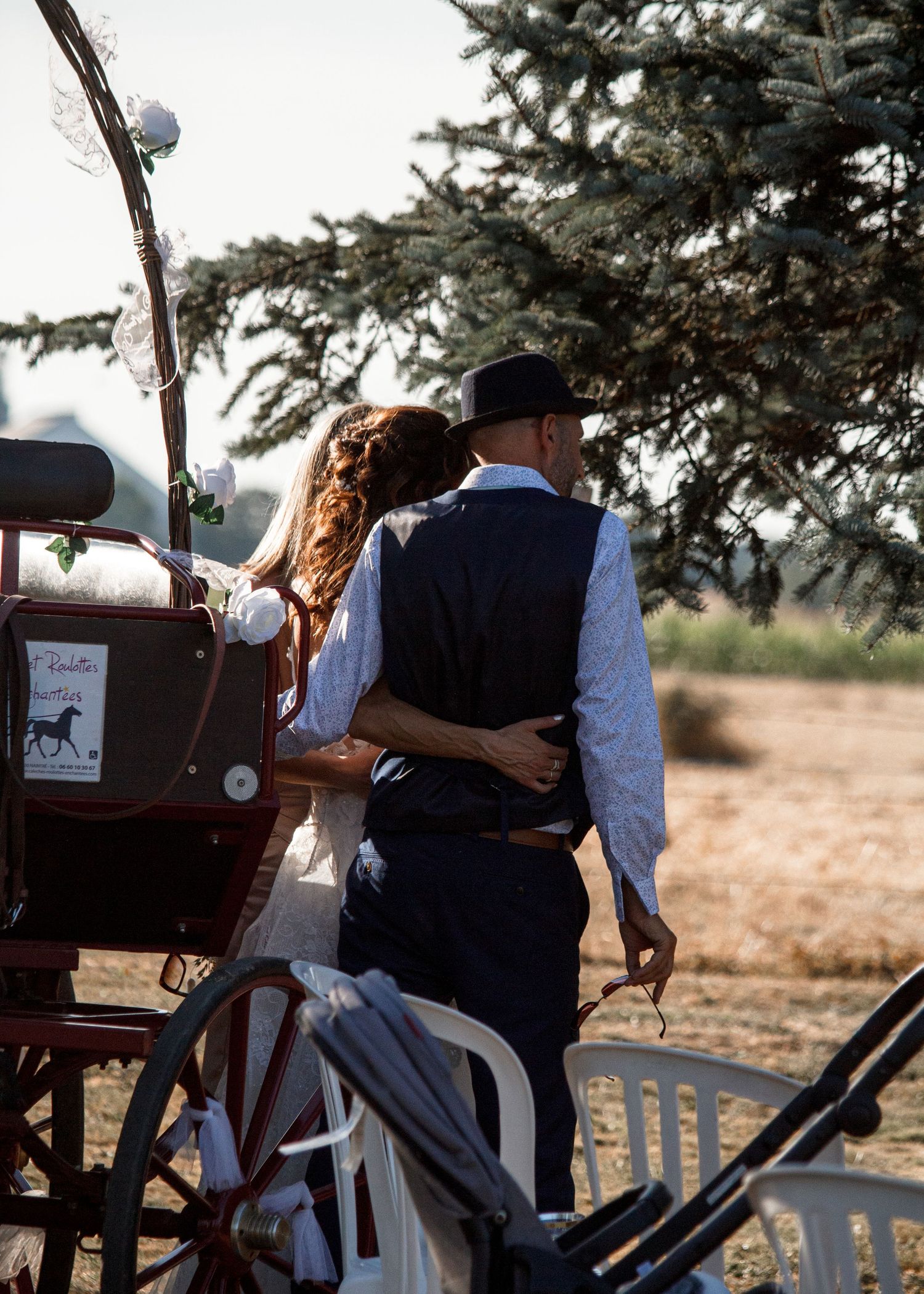 Couple enjoying a romantic wagon ride through a rural landscape at sunset with trees in the background.