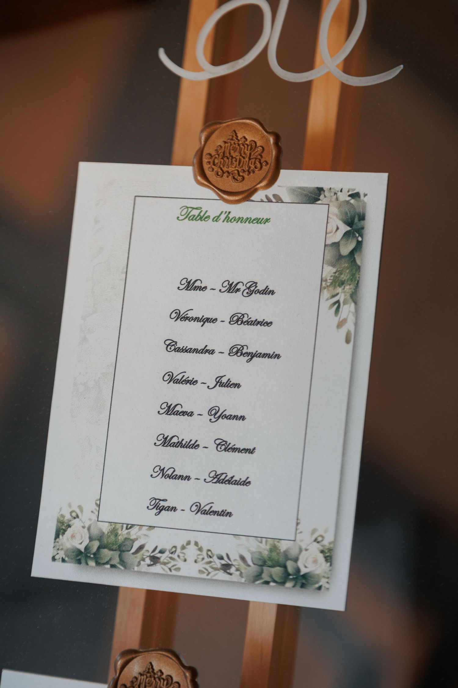 Elegant wedding seating chart on decorative easel with wax seal, listing table assignments in French.