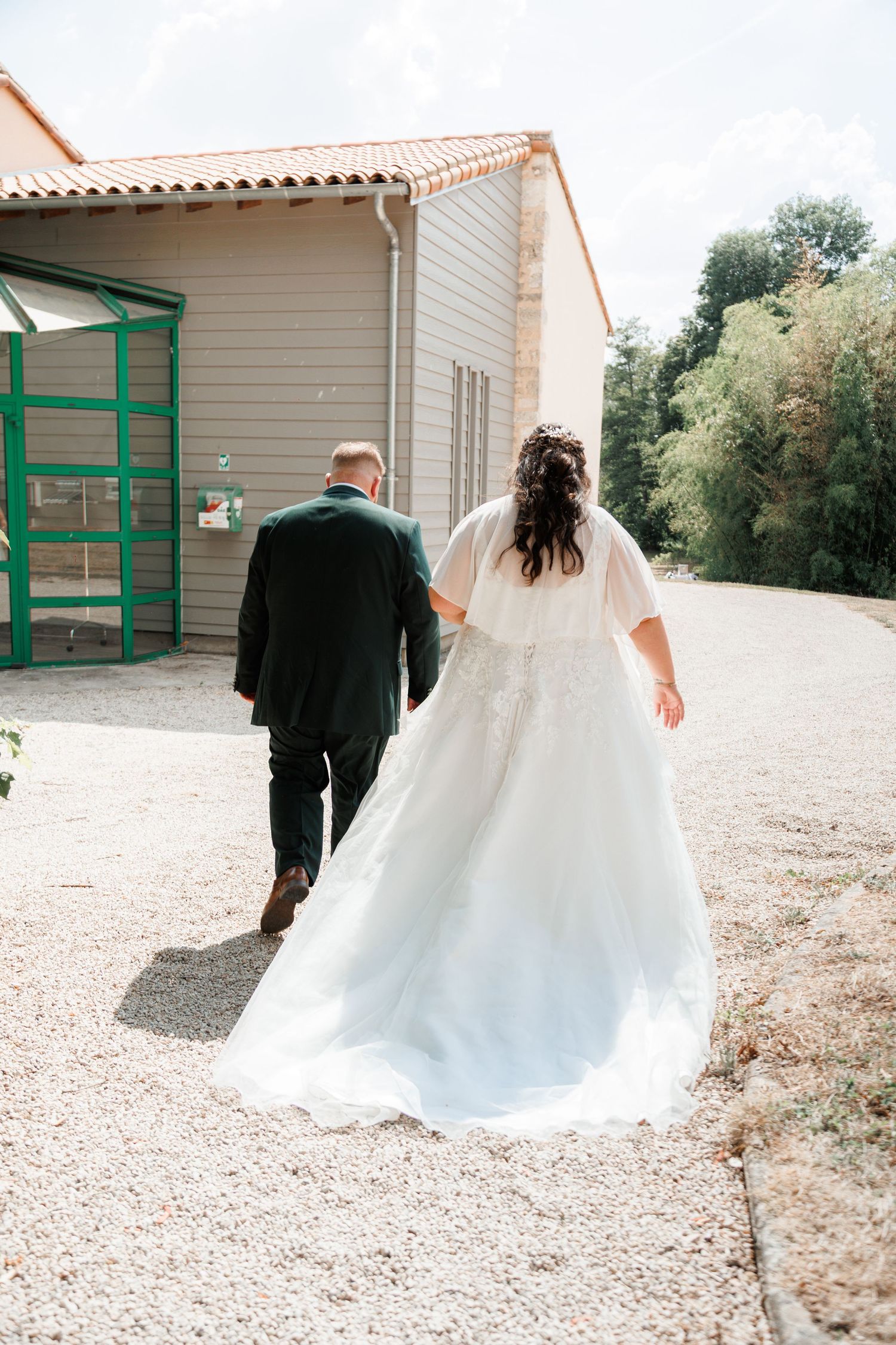 Bride in white gown and groom in dark suit walking away toward a building on their wedding day.