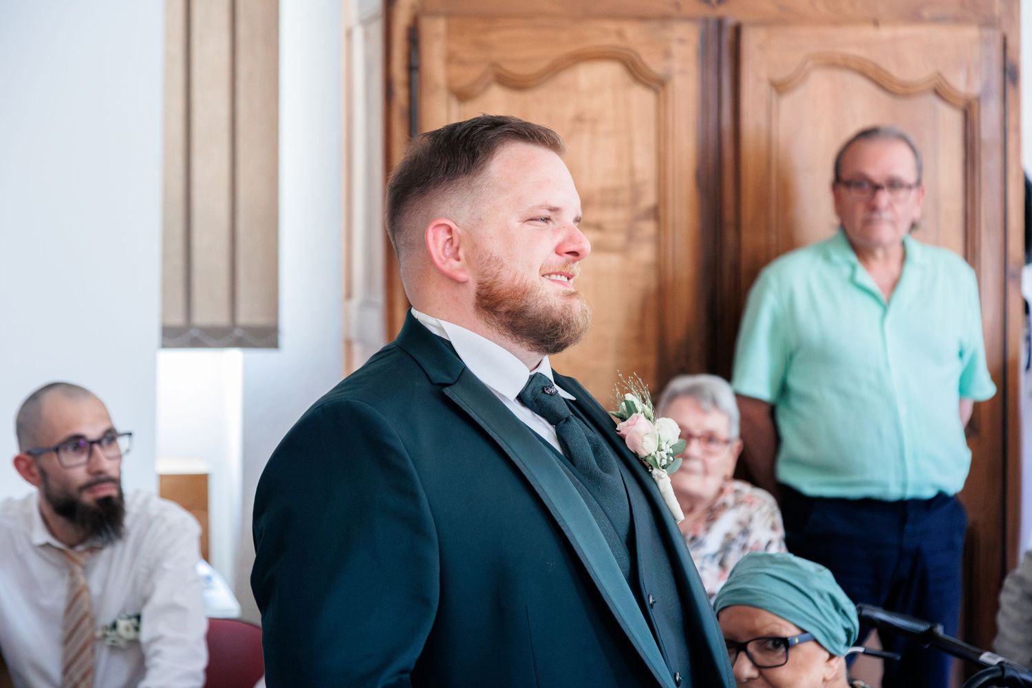 Emotional groom in dark green suit with boutonniere standing at the altar during wedding ceremony.