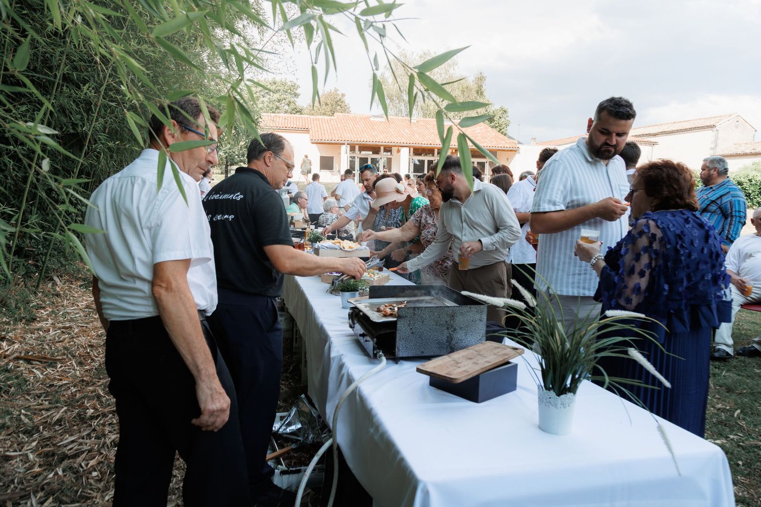 Guests serving themselves food at an outdoor buffet table with white tablecloth at a garden party.