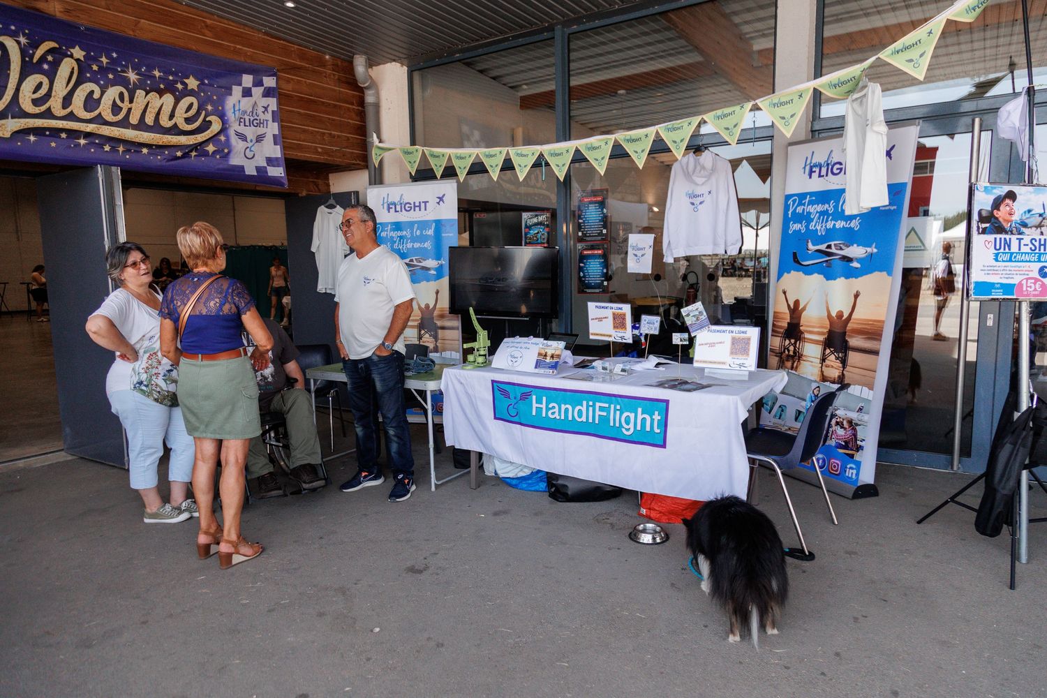 HandiFlight booth at an outdoor event with visitors browsing informational displays and banners at a welcome area.
