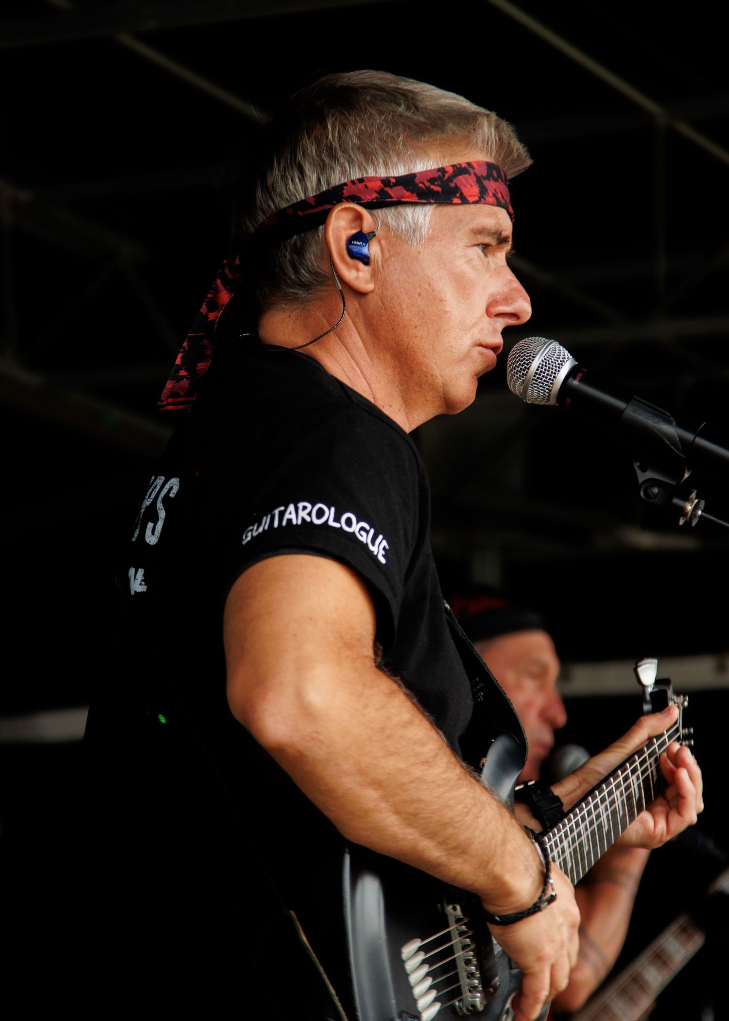 Bassist playing on stage wearing black attire with in-ear monitors during a performance.