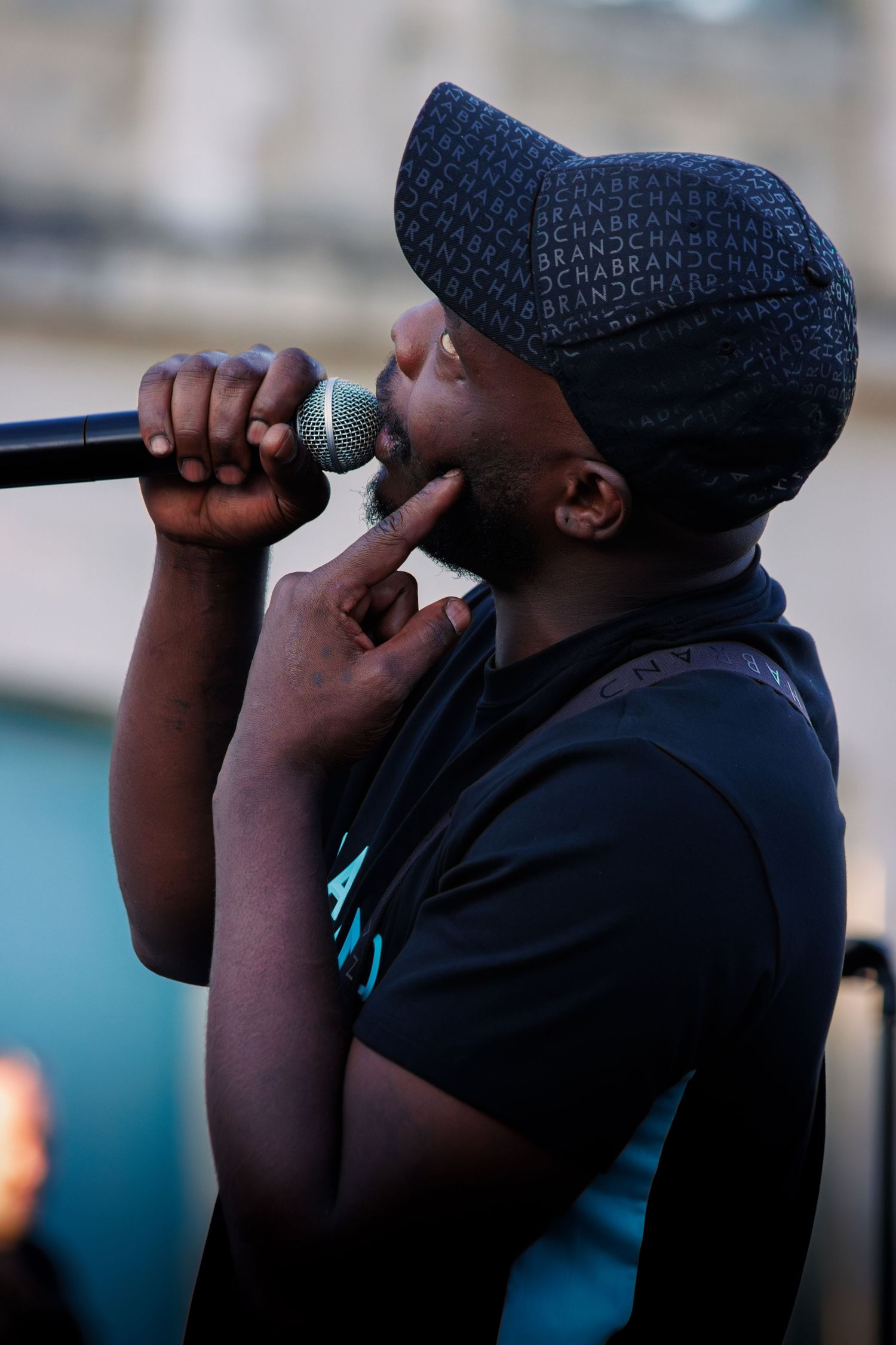 Performer in black cap and t-shirt passionately singing into microphone on stage.