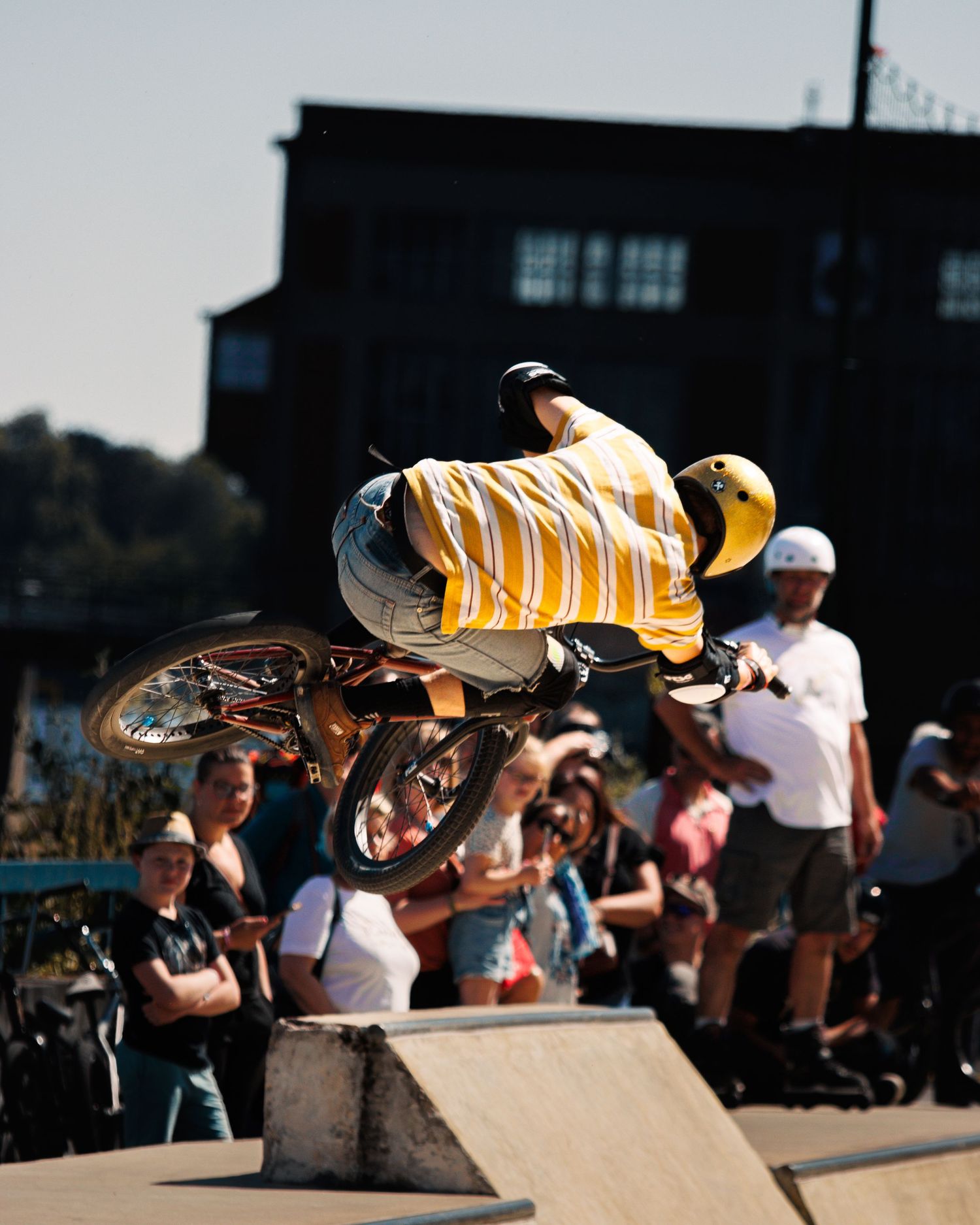 Airborne BMX rider performing trick above ramp with crowd watching.