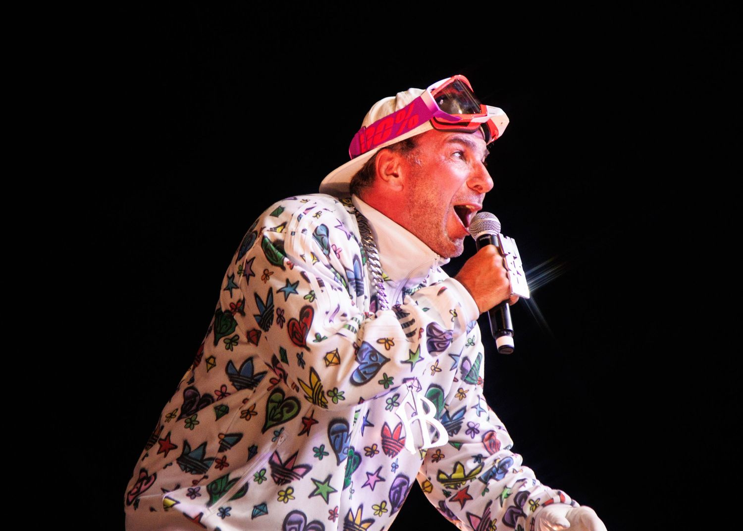 Someone performs on stage wearing a colorful patterned shirt and red baseball cap while holding a microphone.