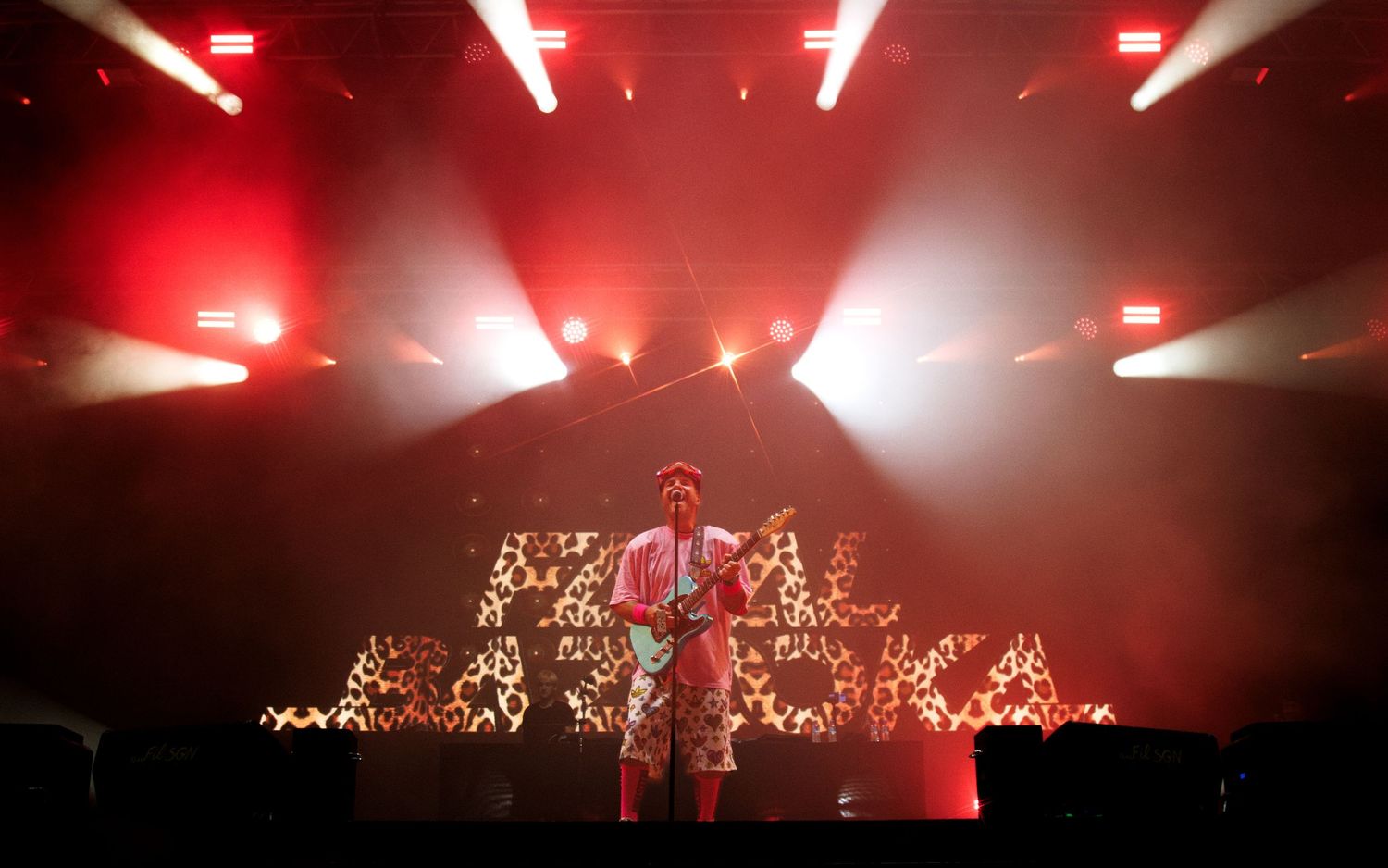 Concert stage illuminated with dramatic red lighting and fog effects creating an atmospheric performance environment.