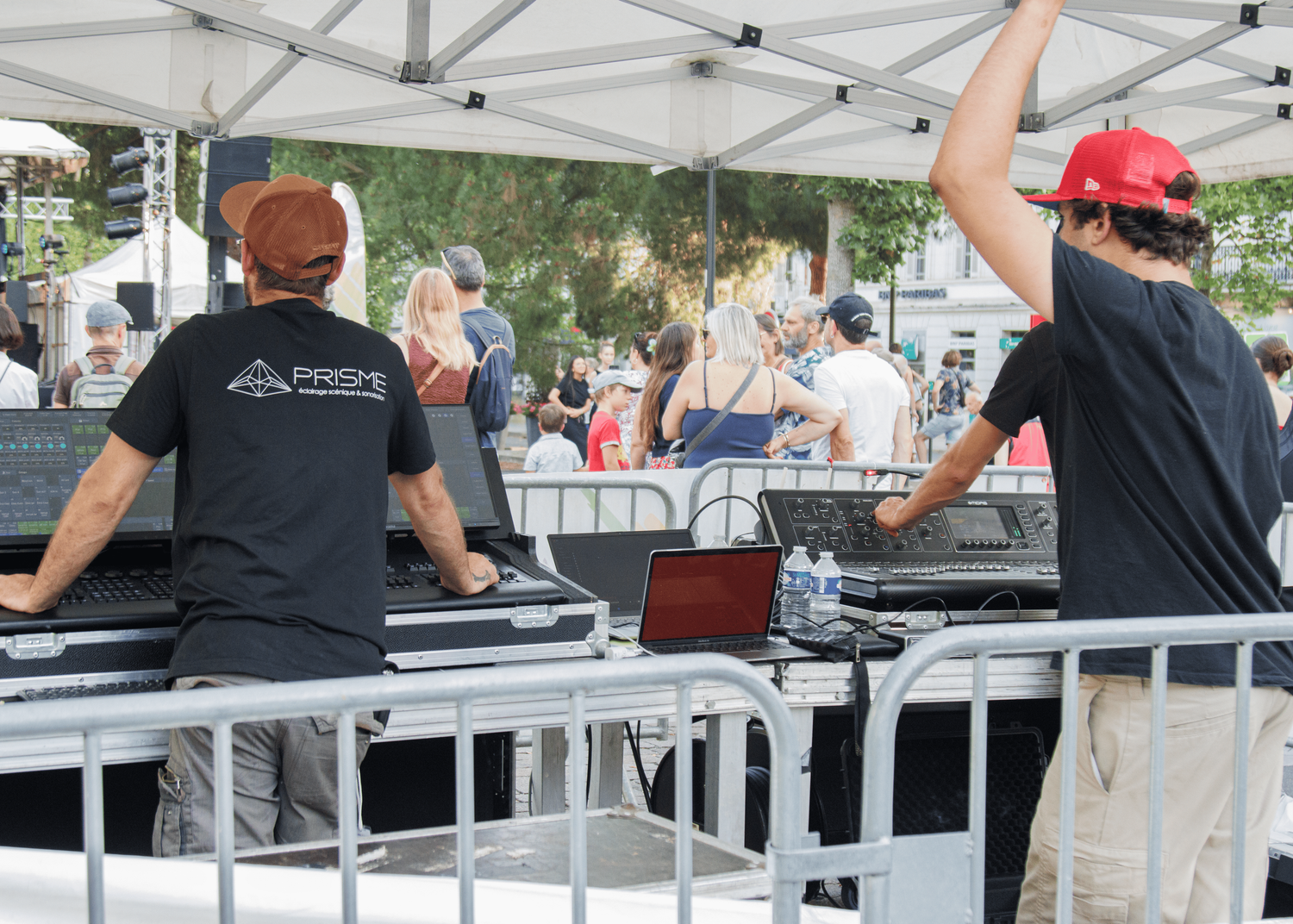 Black sound equipment and mixing boards arranged under a white tent at an outdoor event.