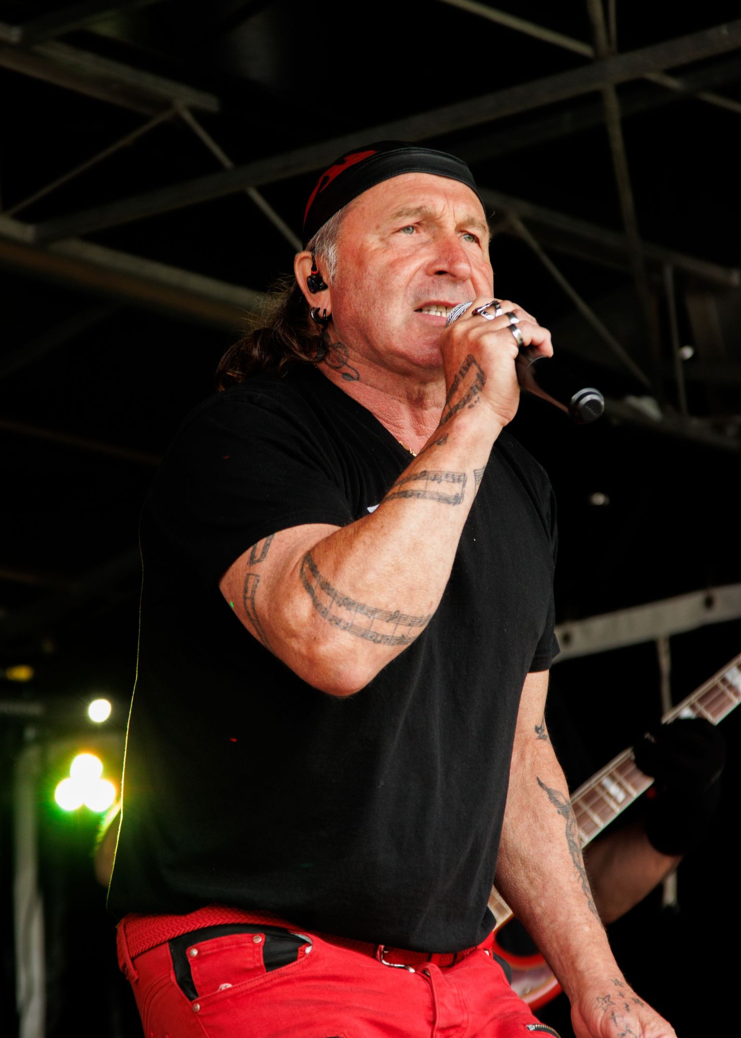 Performer in black shirt and red pants singing on stage with dramatic lighting.