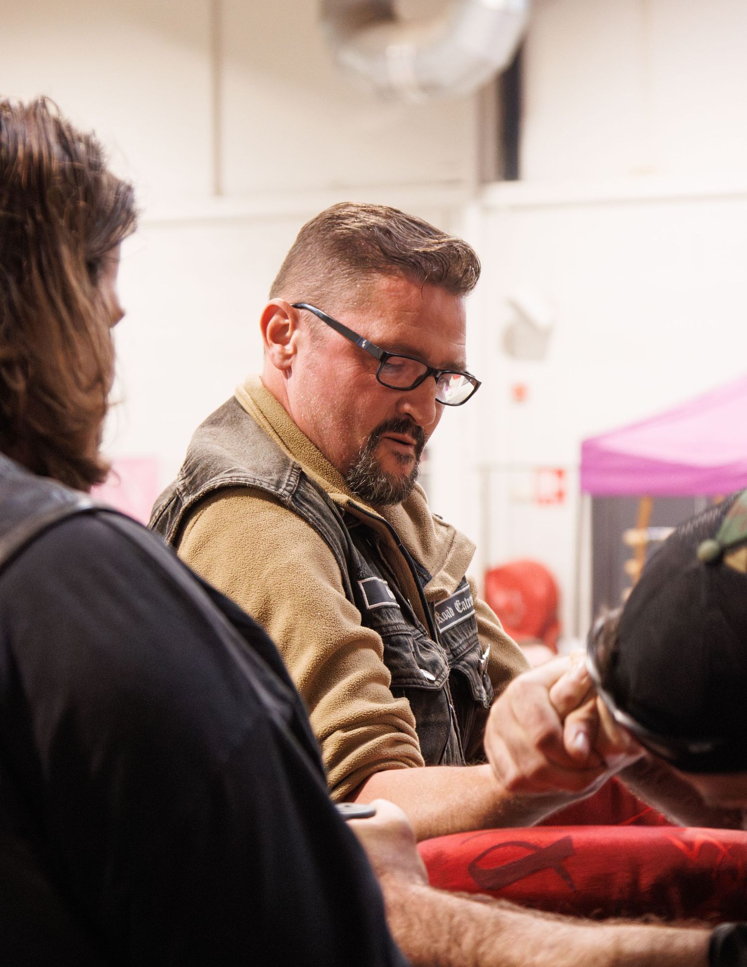 Person in tan vest and glasses participates in indoor event.