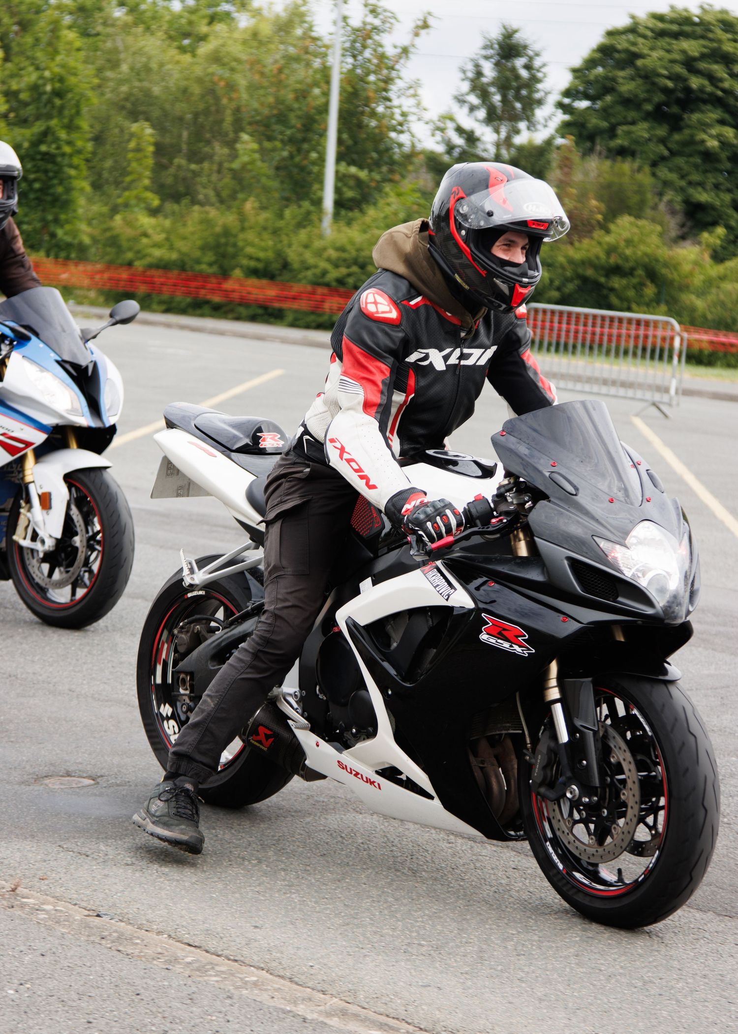 Rider in full racing gear mounted on black and white sports motorcycle in parking area.