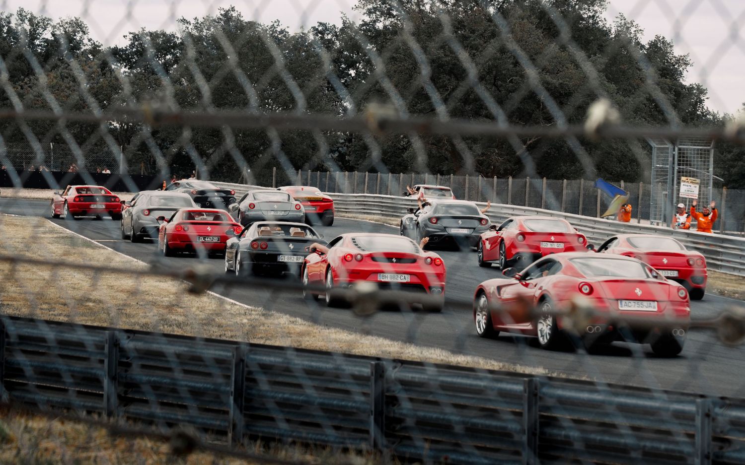 Multiple vintage Ferrari sports cars line up along race track barrier during event.