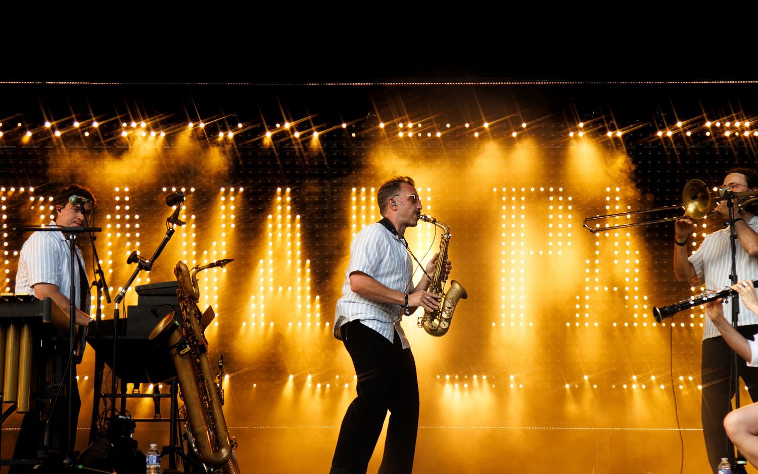 Musician playing saxophone on stage with golden LED lights and dramatic yellow lighting at a live concert performance.