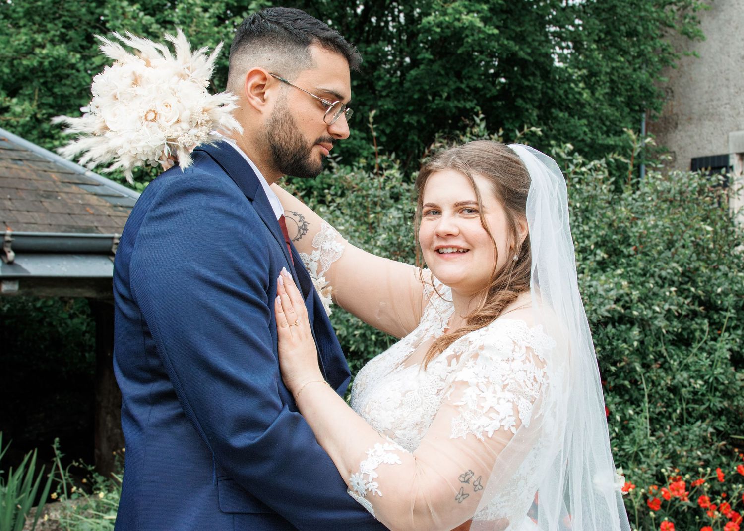 A bride and groom share a tender moment outdoors, with the bride in a lace veil and the groom in a navy suit.