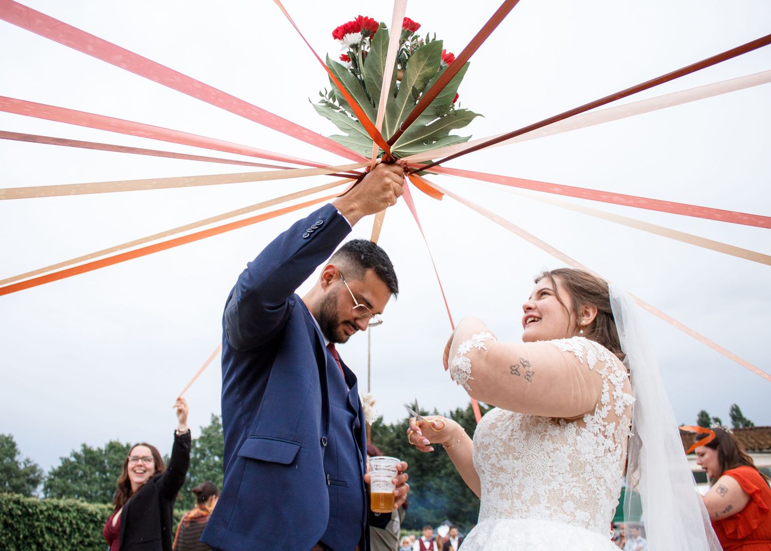 Joyful bride and groom hold colorful ribbons bouquet aloft during outdoor wedding ceremony celebration.