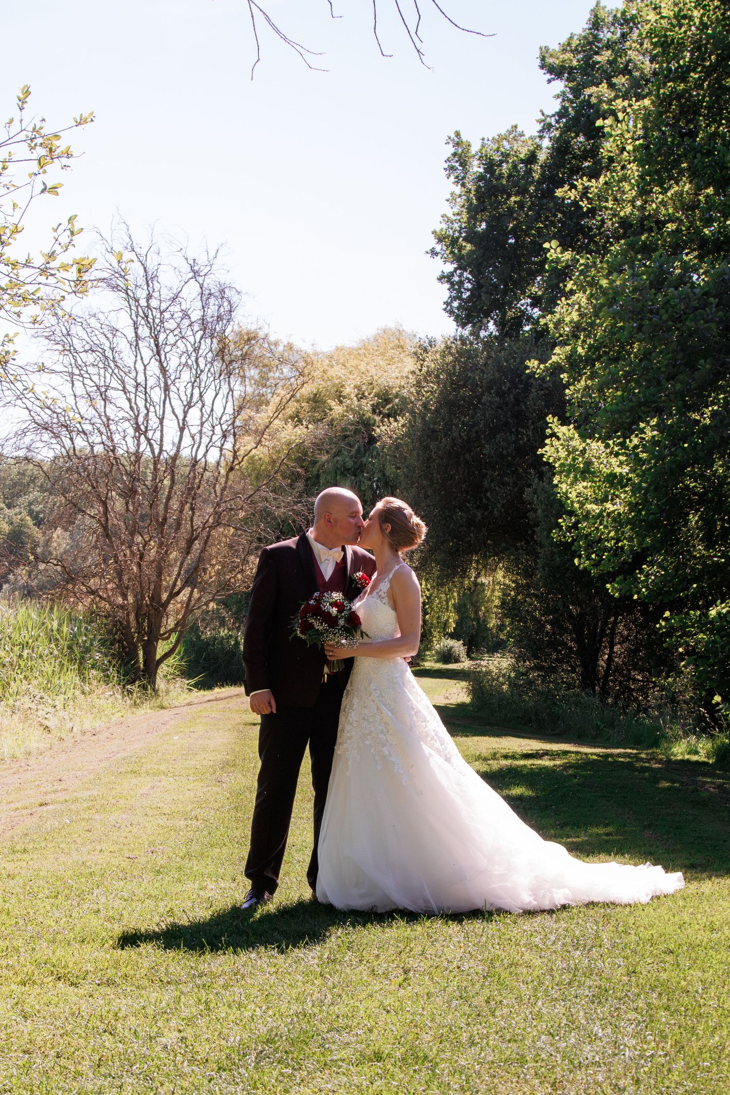 Bride and groom sharing a kiss in a lush garden on their sunny wedding day.