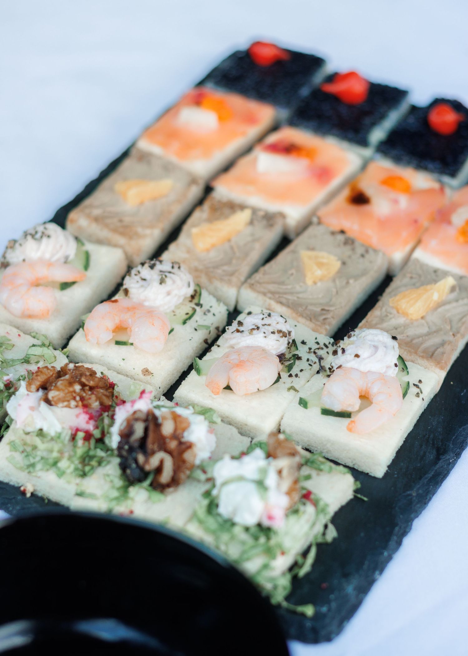 Elegant wedding appetizers displayed on slate board featuring shrimp, salmon, and assorted toppings.