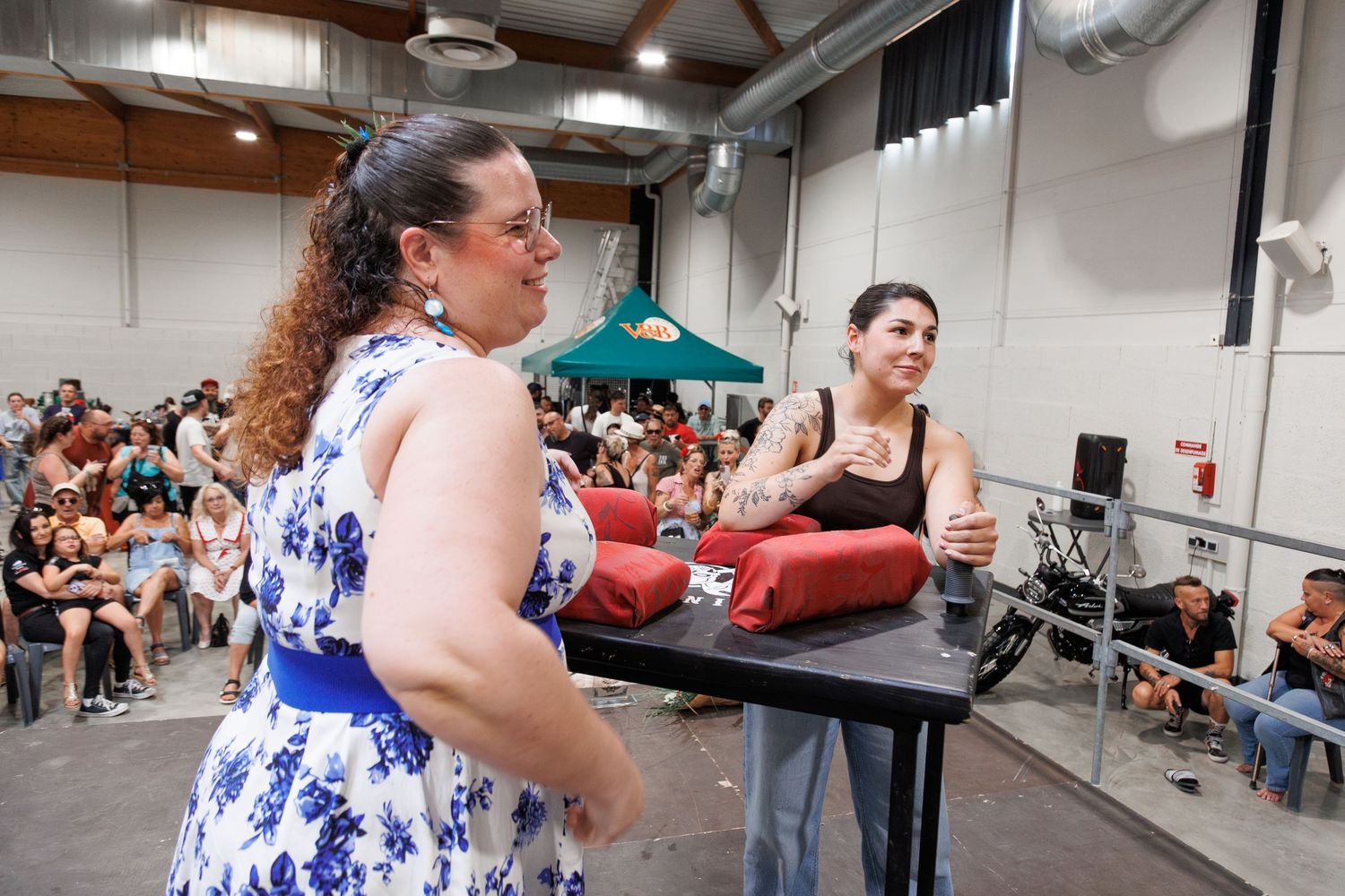 Two women on stage at a crowded indoor event, one in a floral dress holding red boxing gloves.