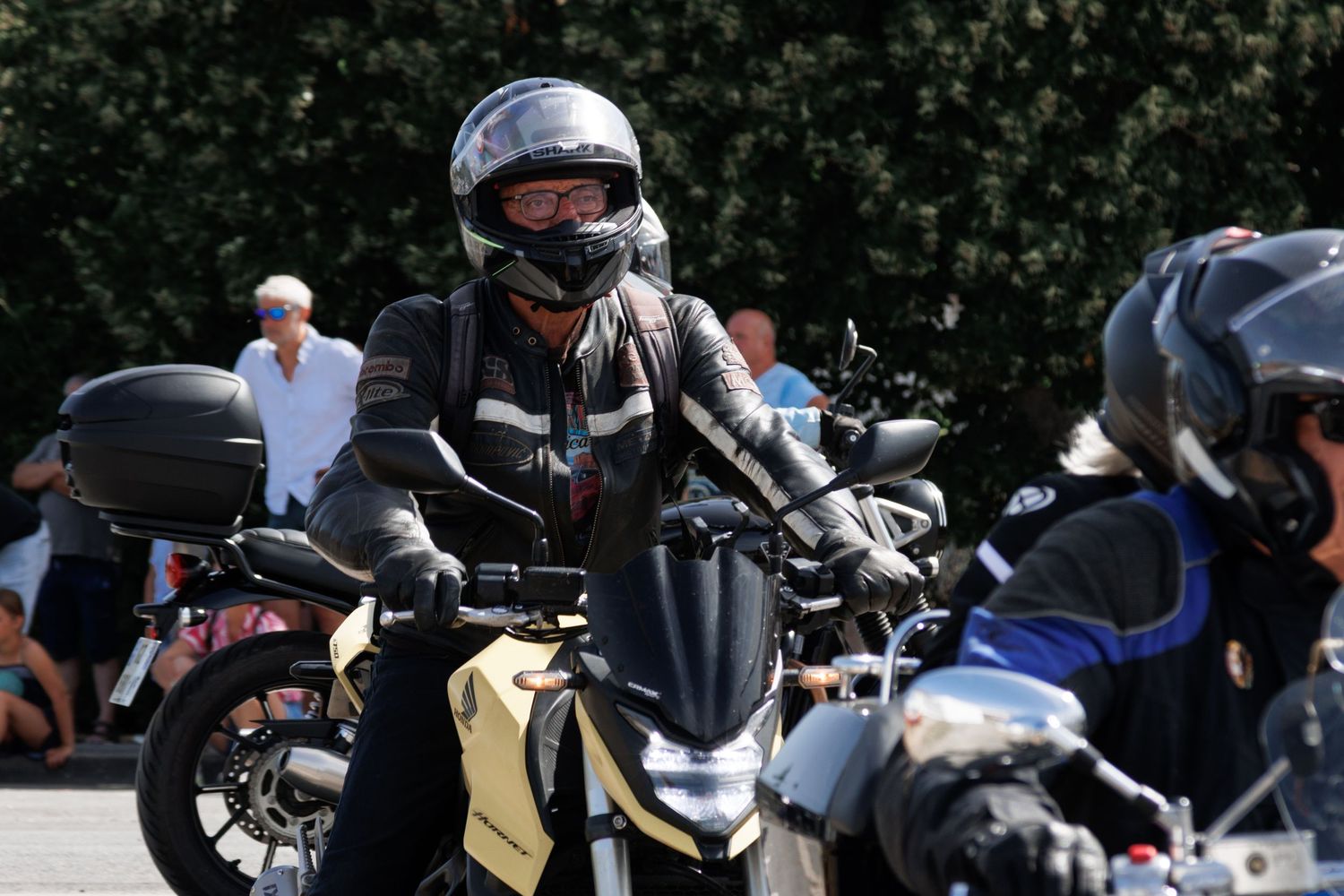 Motorcyclist in helmet and riding gear on a gold and black motorcycle at an outdoor gathering.