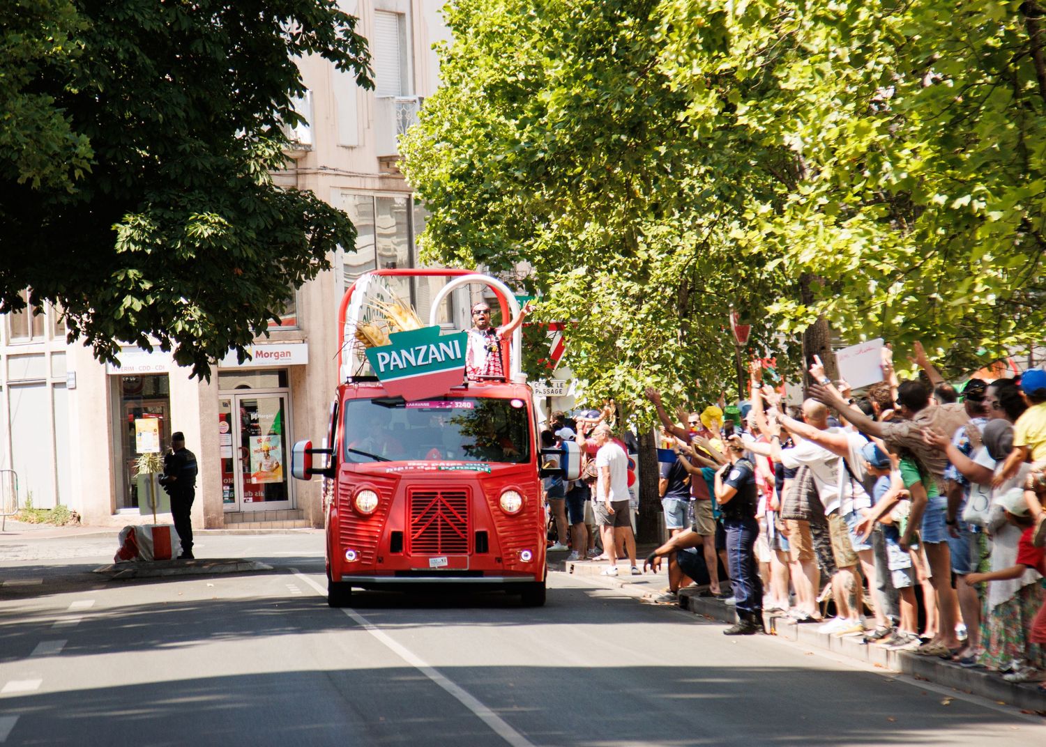 A vintage red promotional vehicle drives through streets lined with cheering spectators.