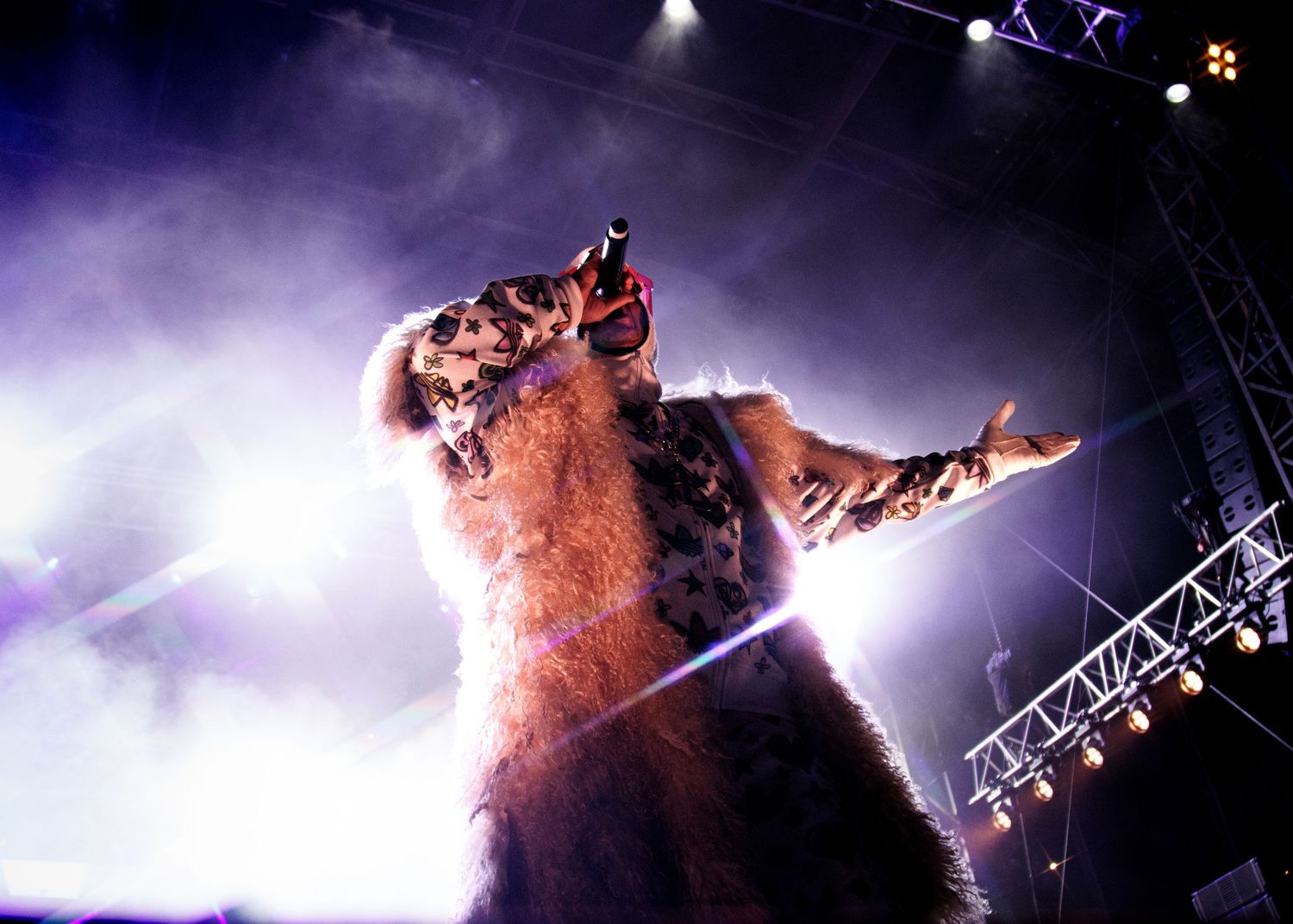 A dramatic concert performance with a figure silhouetted against purple stage fog and theatrical lighting.