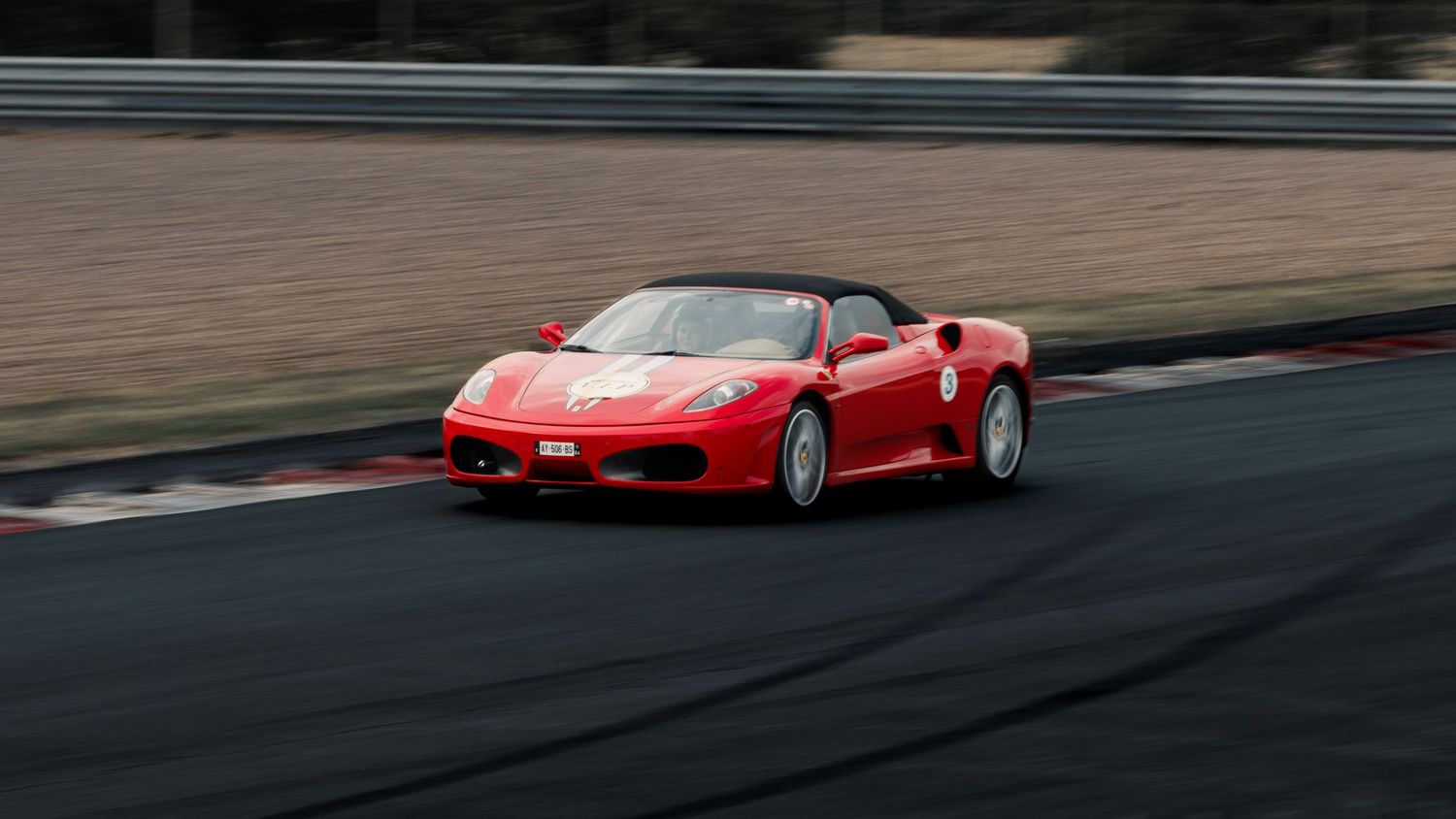Red Ferrari F430 drives through racetrack corner during track session.