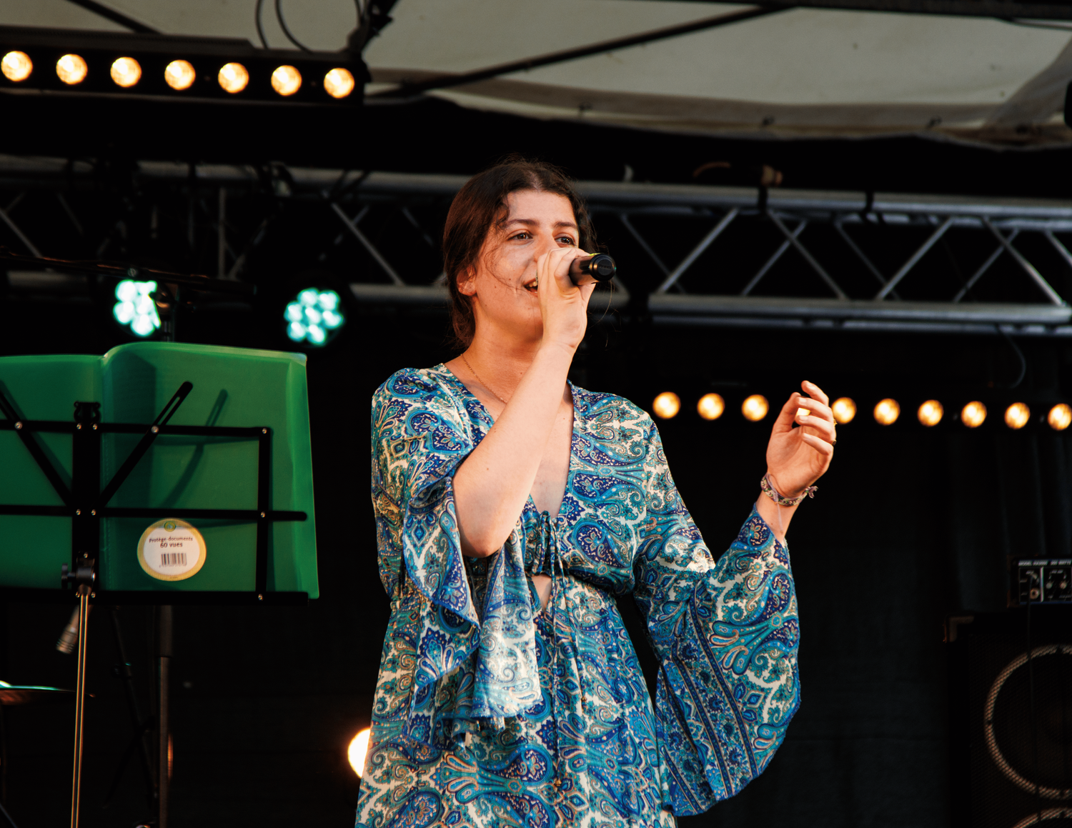 A vocalist performs emotively on an outdoor stage with dramatic lighting.