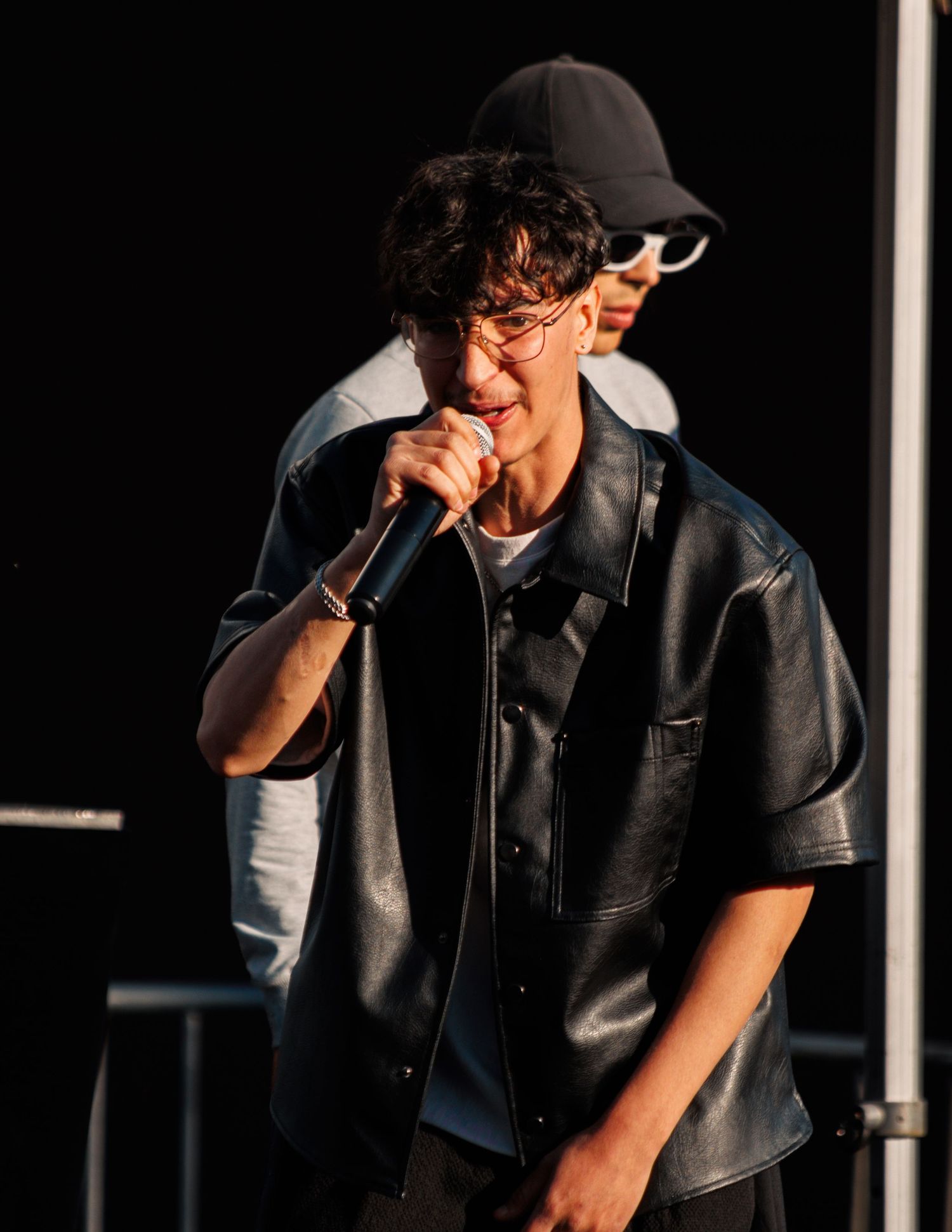 Performer in black leather vest holds microphone during outdoor show.
