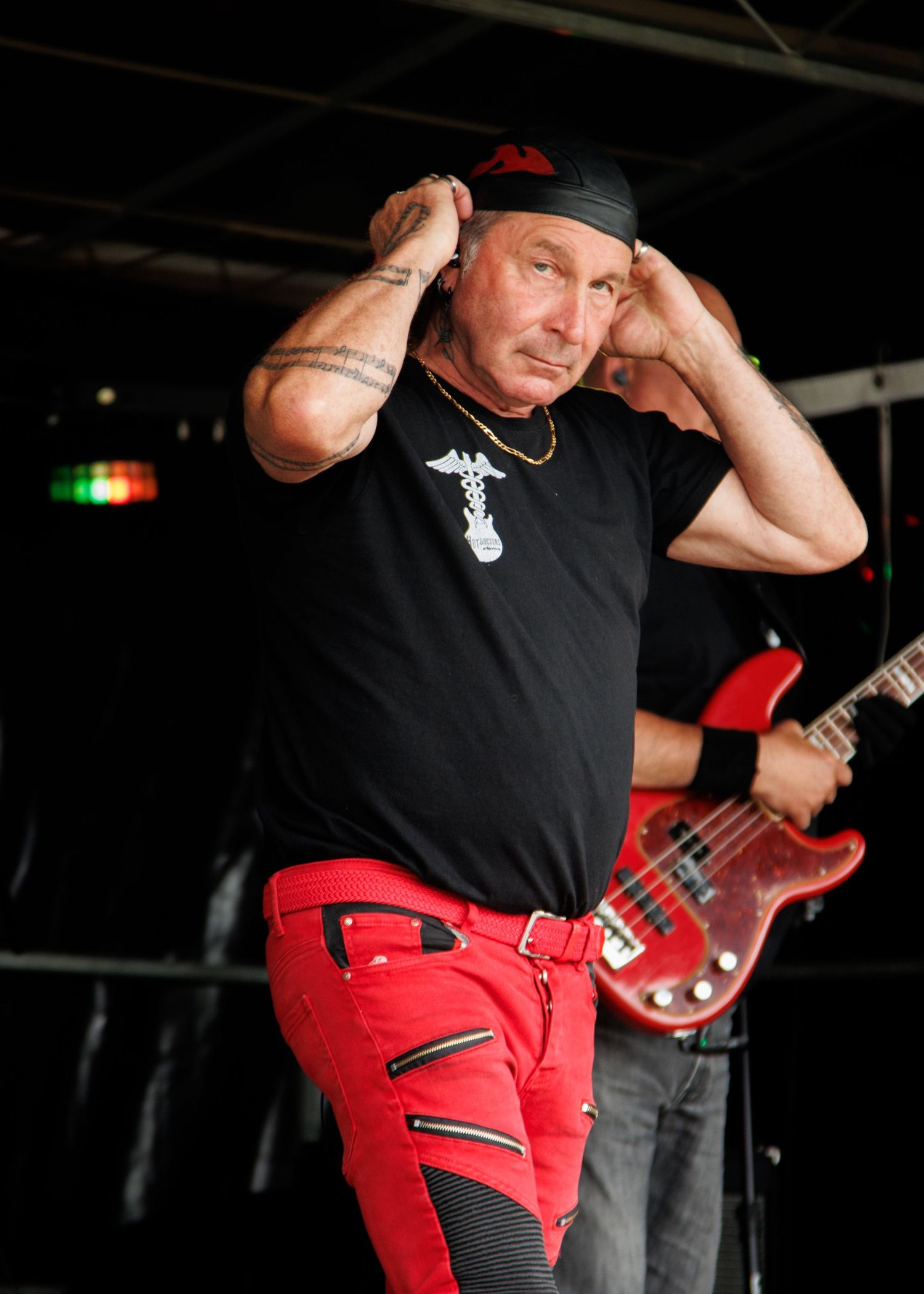 Rock performer in black shirt and red pants adjusting cap during live performance on stage.