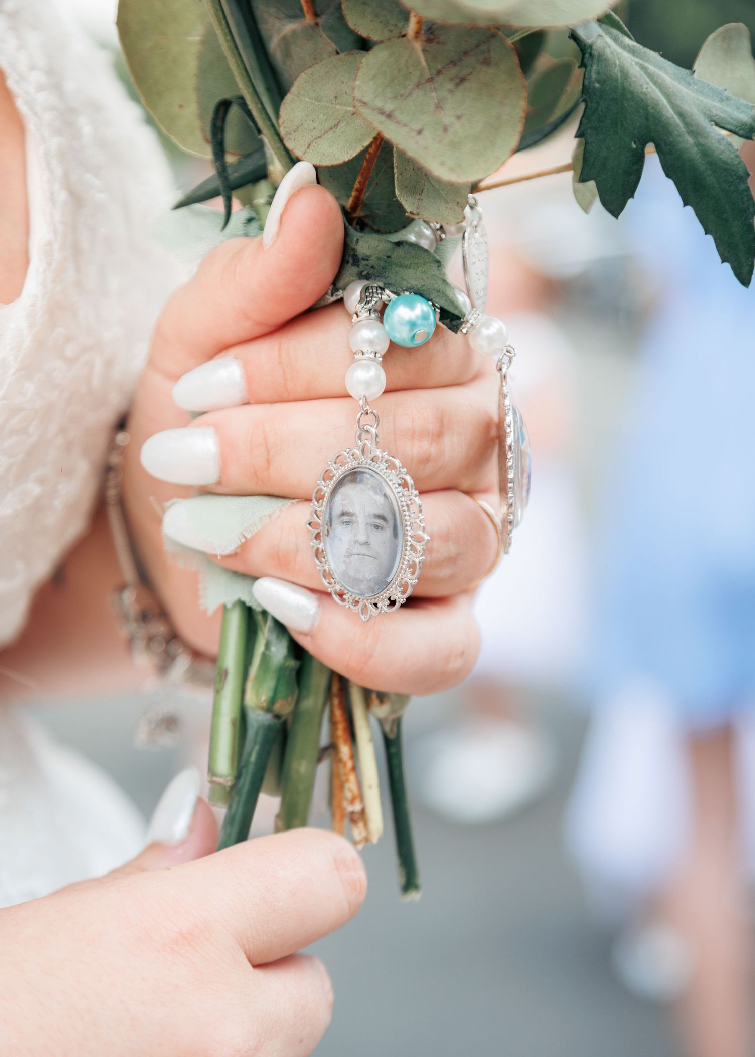 Bride holds bouquet with a memorial photo charm pendant honoring a loved one on her wedding day.