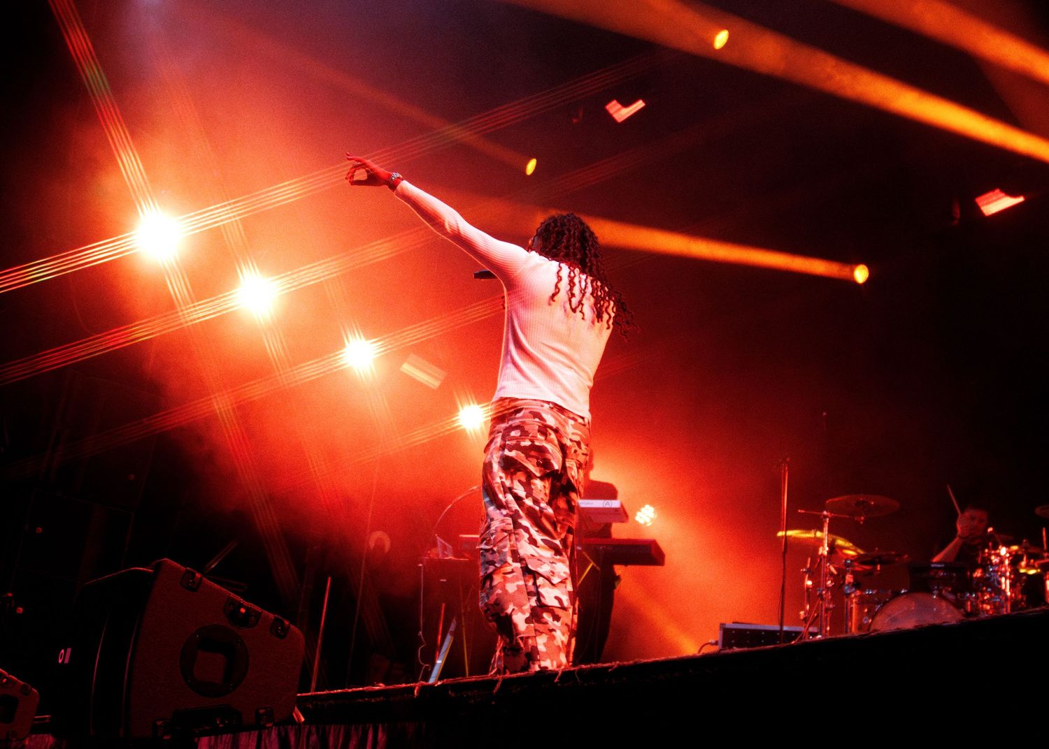 Performer on stage with arms raised under dramatic red and orange stage lighting at a live concert.