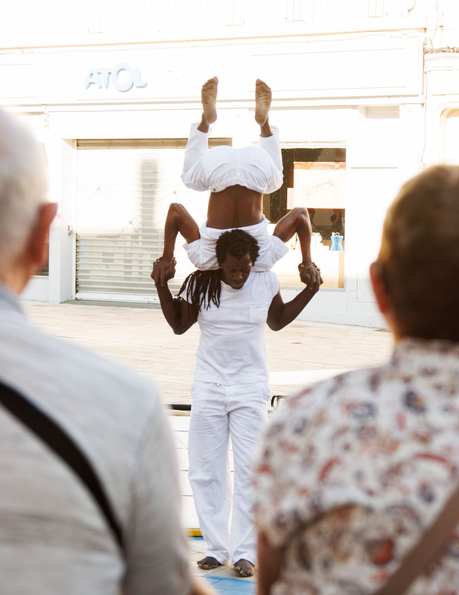 Acrobats in white outfits perform a balancing stunt during an outdoor street performance.