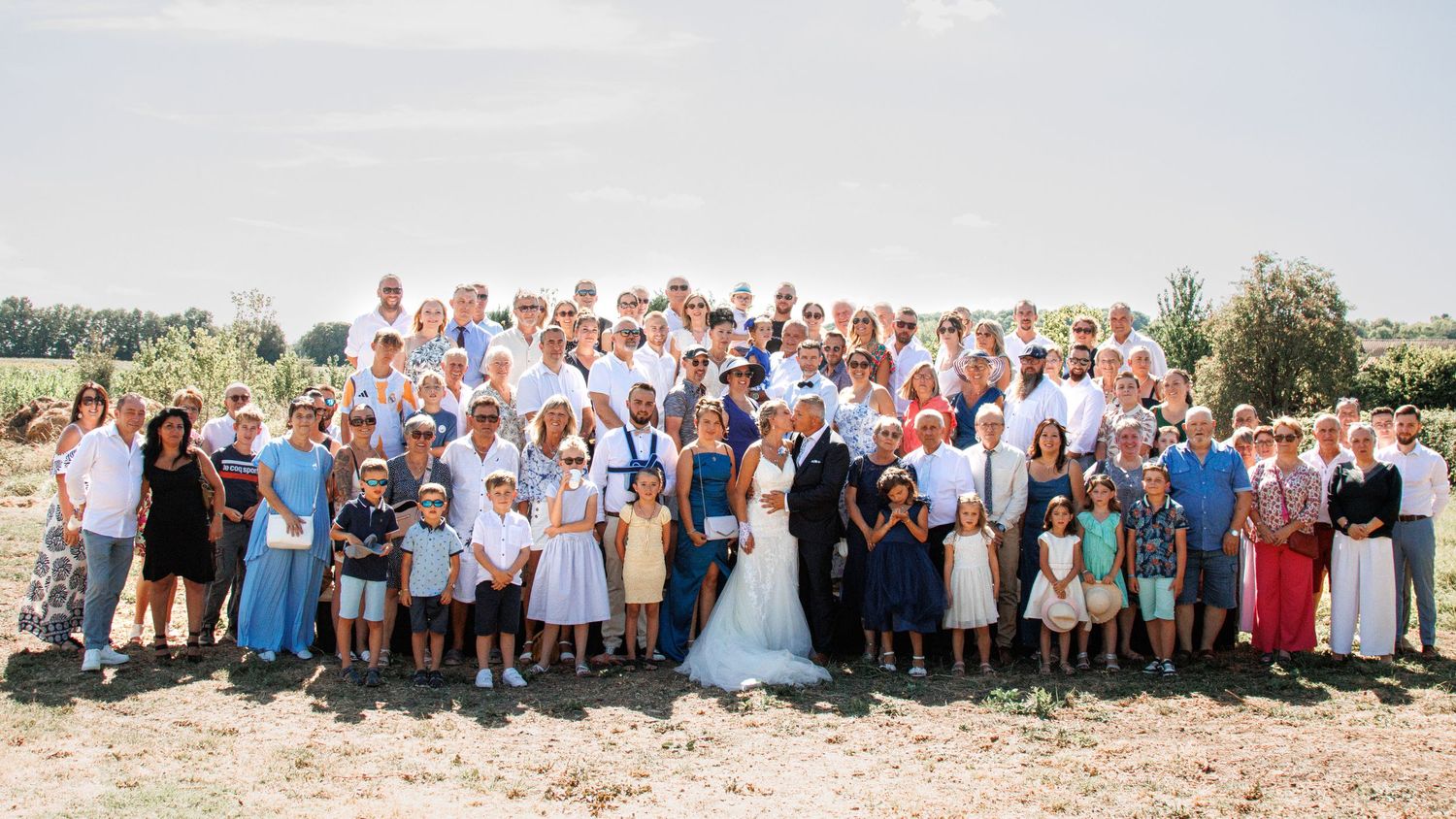 Large group wedding photo with attendees in blue and white attire gathered outdoors.