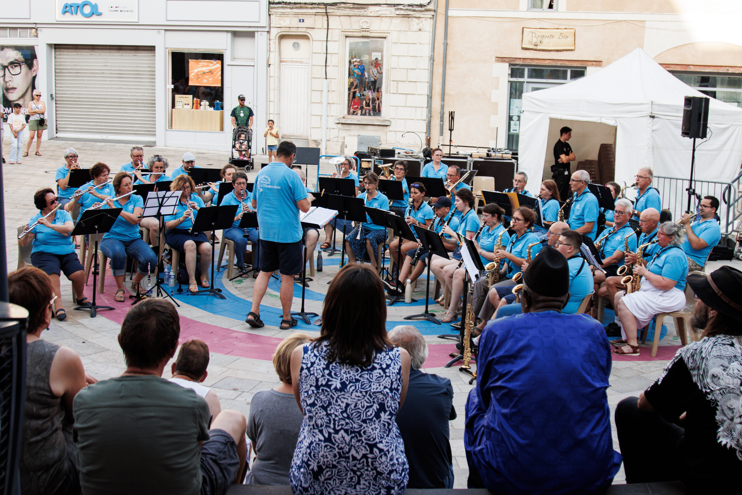 A youth band in bright blue shirts performs outdoors while an audience watches from folding chairs.