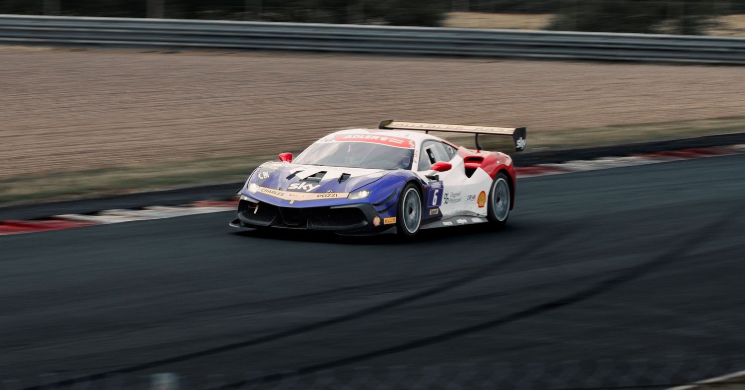 White and blue Ferrari race car navigates track corner at high speed.
