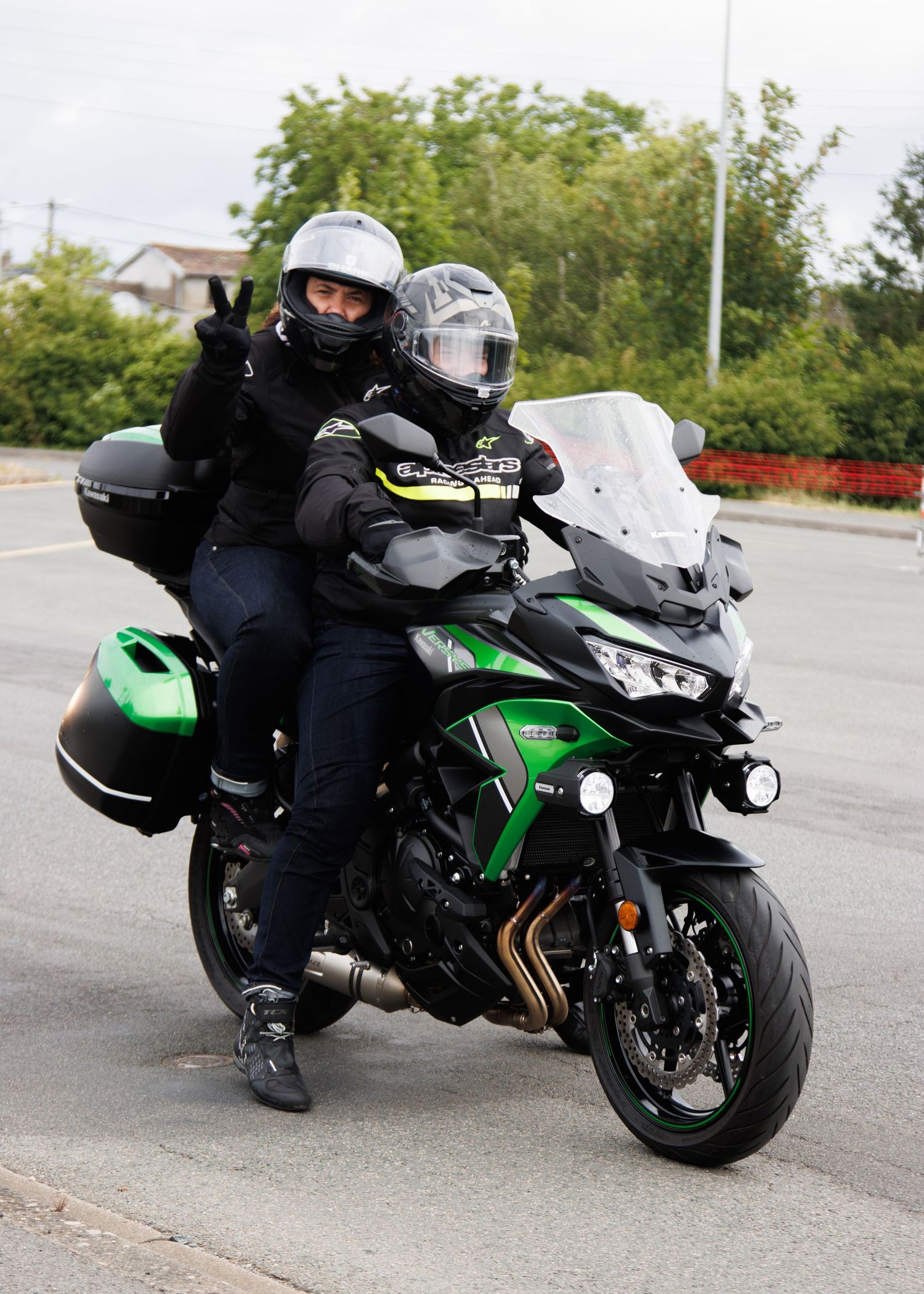 Riders on green Kawasaki motorcycle with luggage cases stopped on asphalt road.