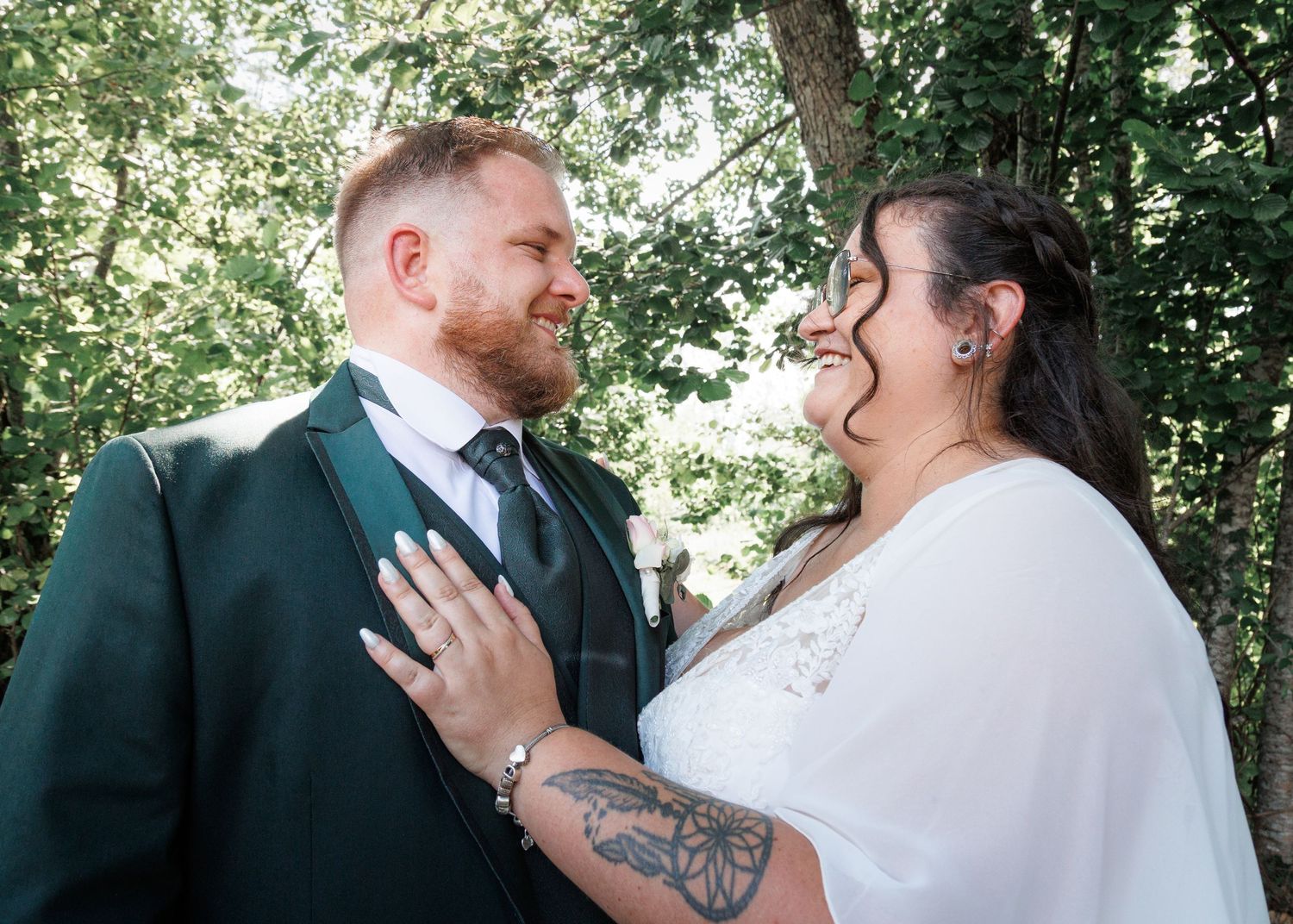 Happy bride and groom sharing a joyful moment together outdoors surrounded by green trees.