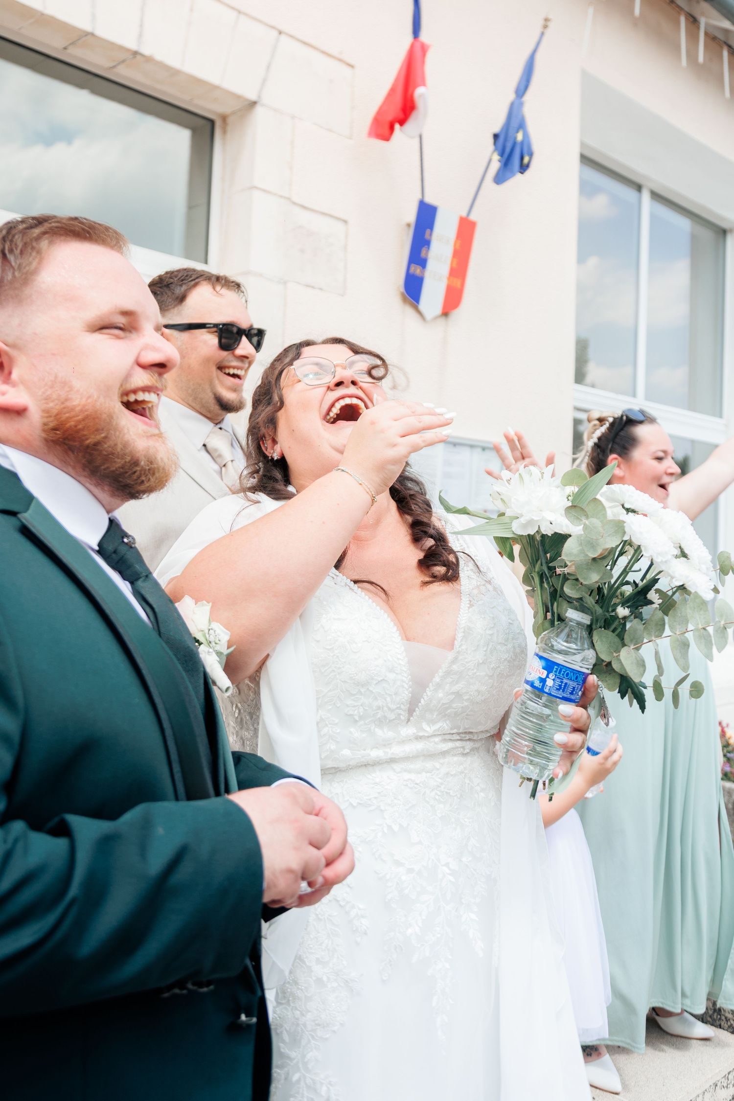 Laughing bride and groom celebrating outside French town hall with wedding party.