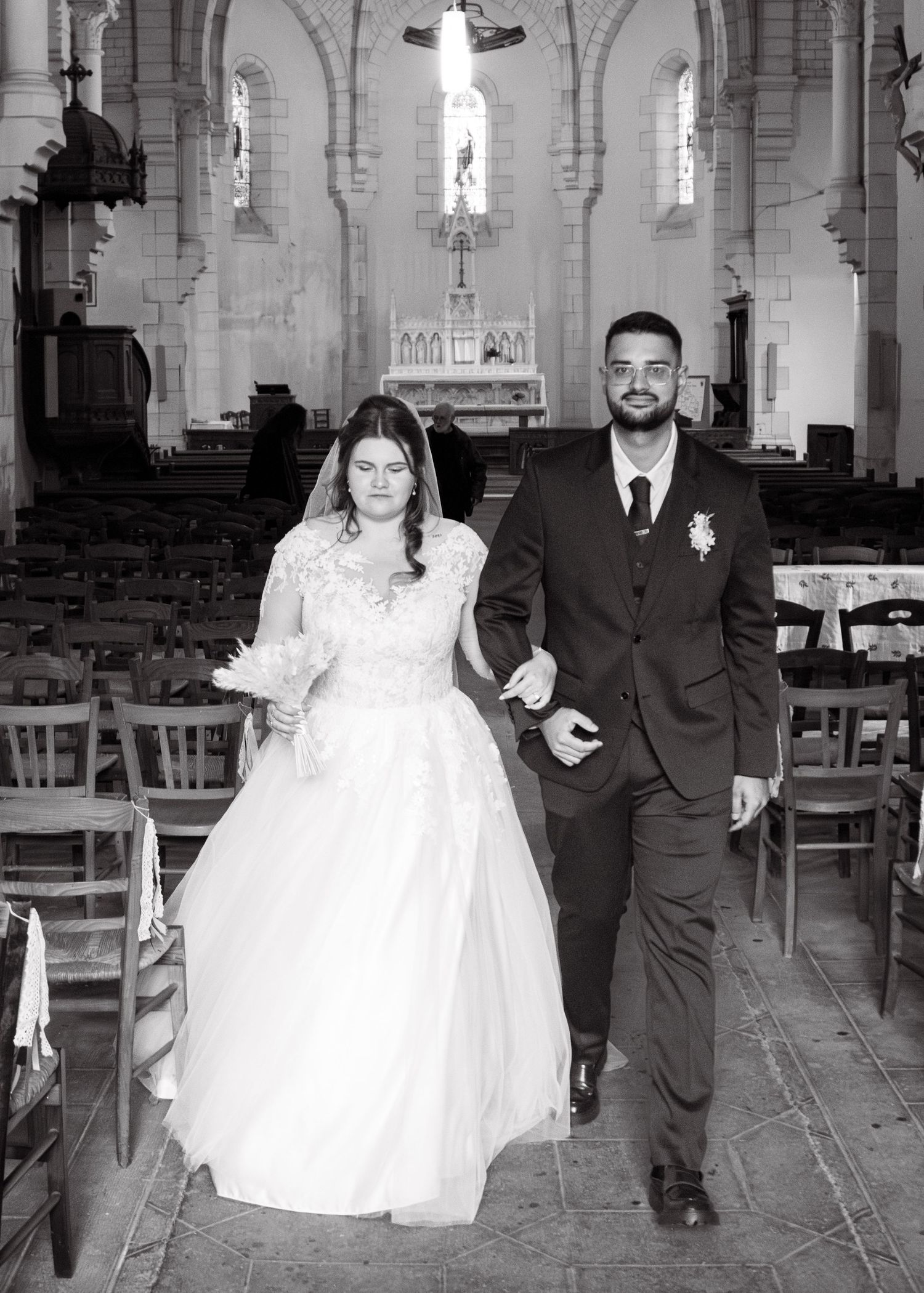 Black and white photo of a bride and groom walking down the aisle of a church after their wedding ceremony.