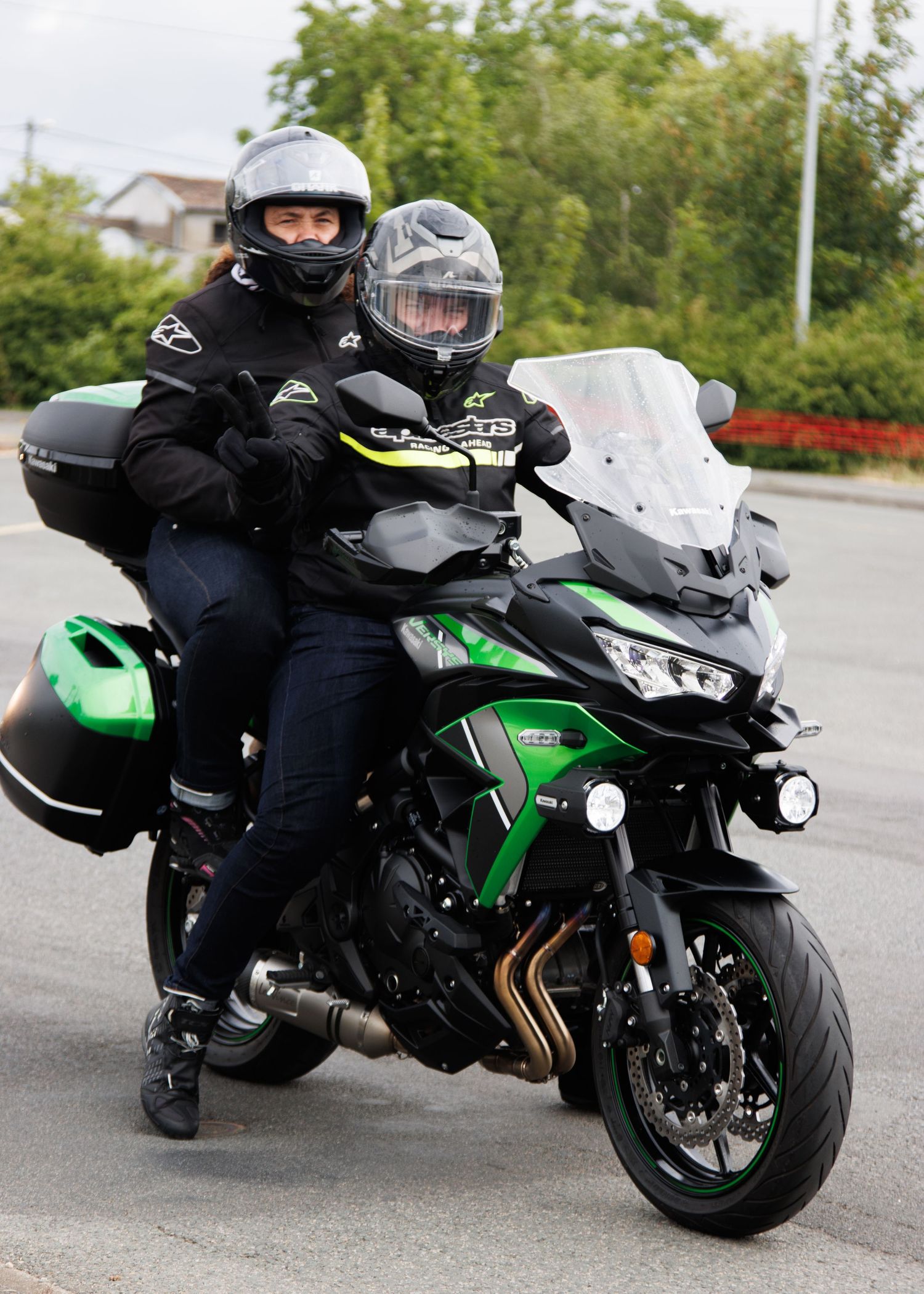 Two riders on a green Kawasaki Versys touring motorcycle in full protective gear.