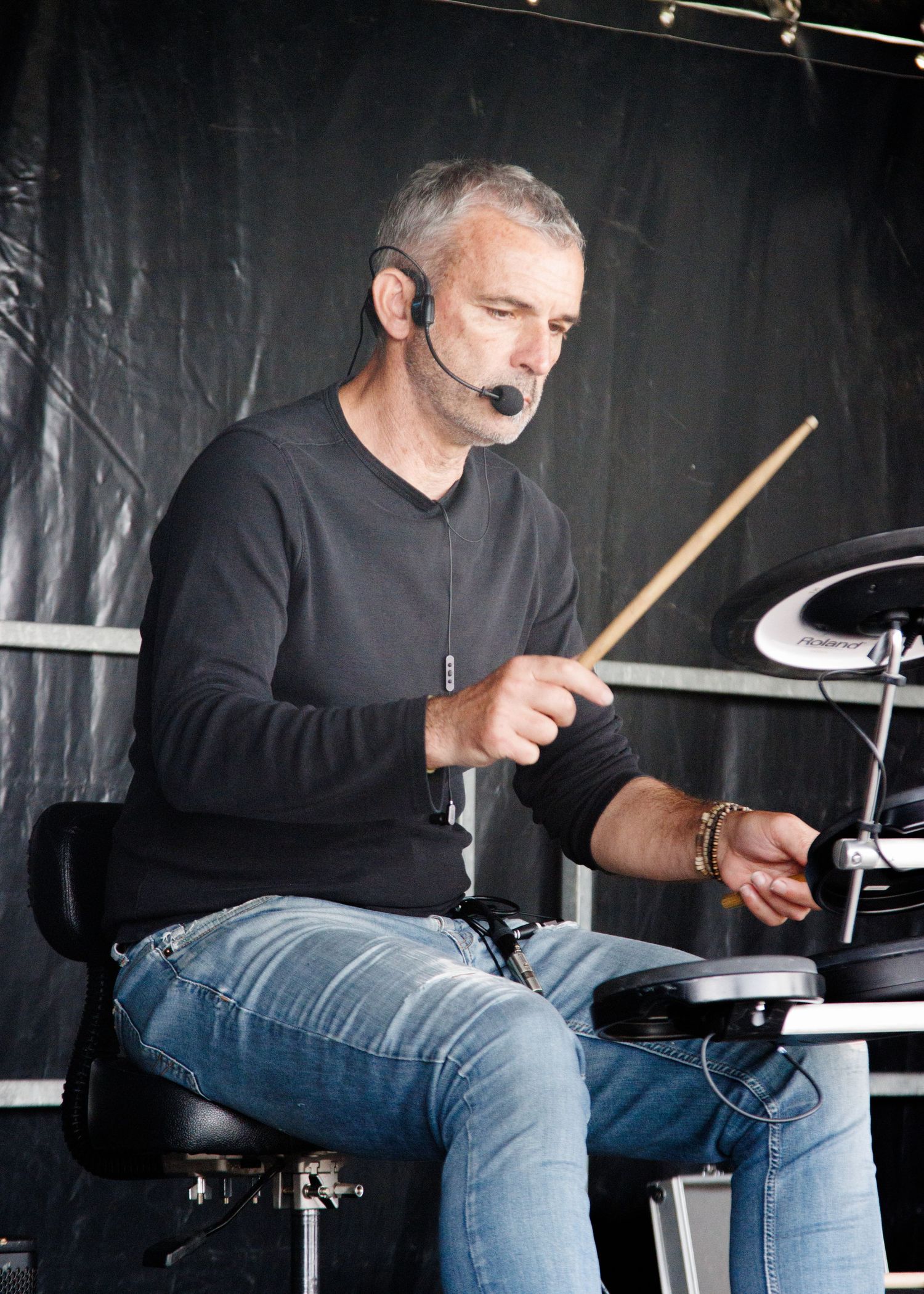 Drummer performing on stage with black curtain backdrop.