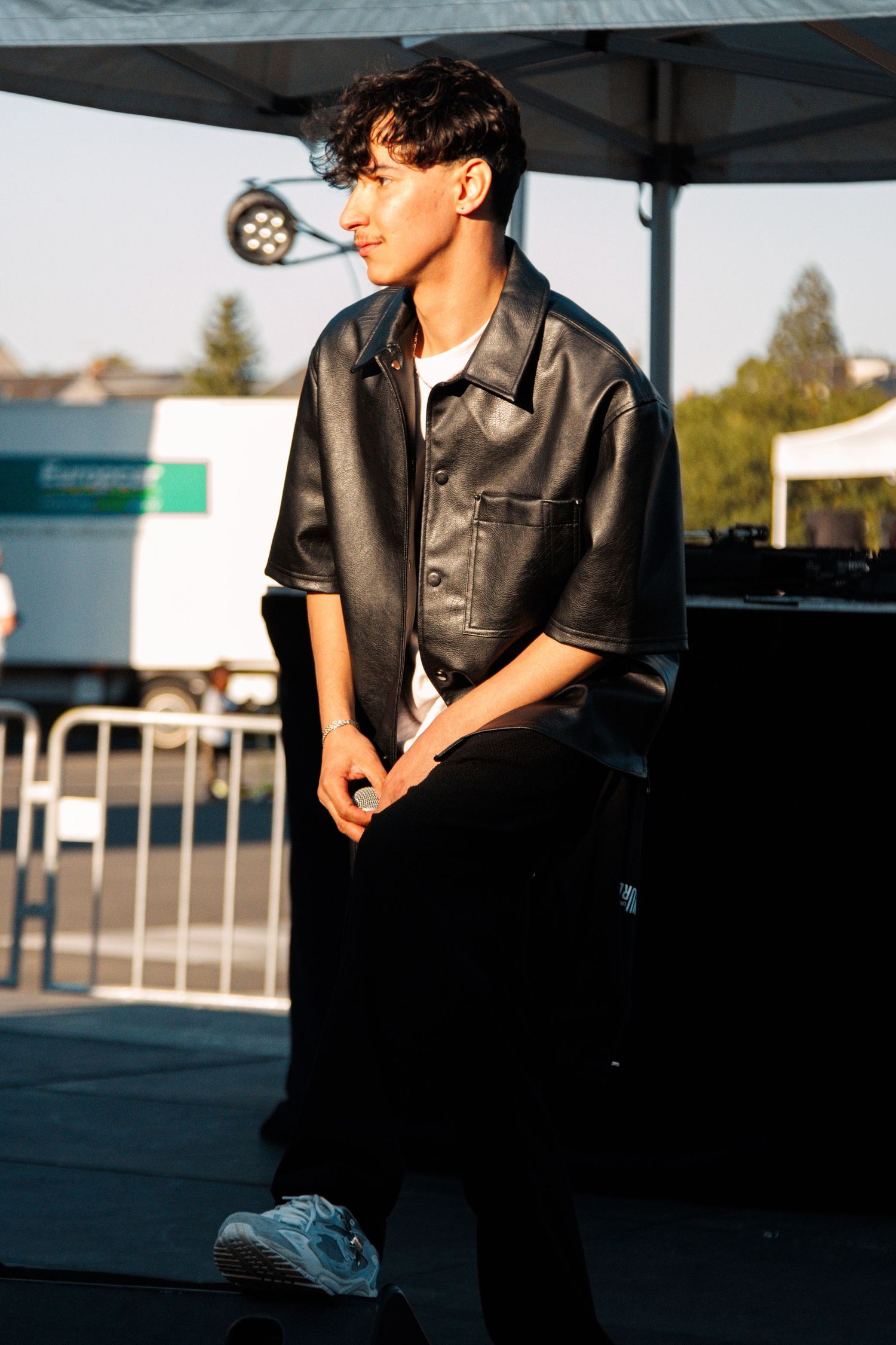 Person in leather jacket poses outdoors under white tent.