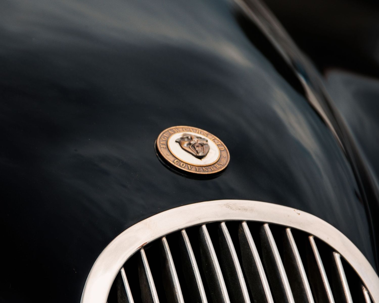 Vintage chrome grille and emblem detail of a classic car against a dark background.