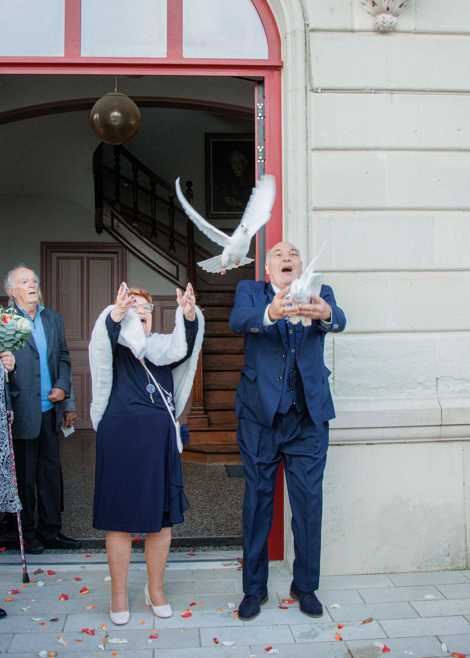 Elderly couple releasing white doves outside a building entrance during a celebration.