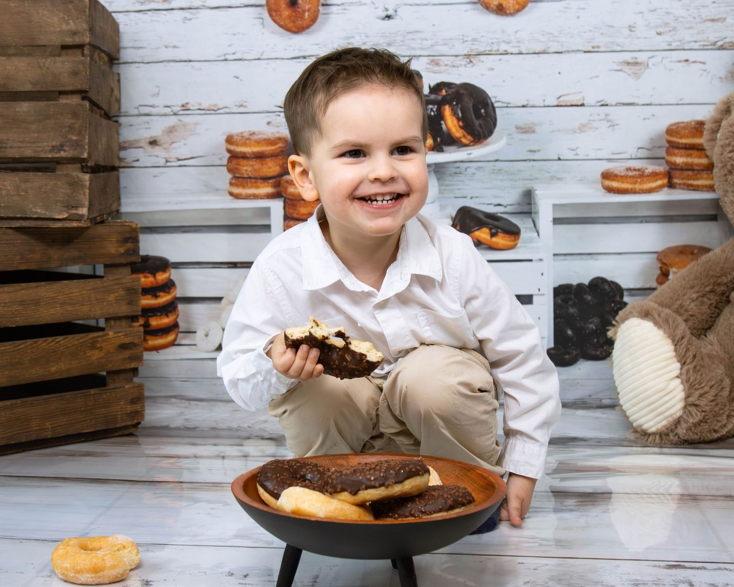 Child in white shirt reaching for treats with wooden crates and donuts in background.